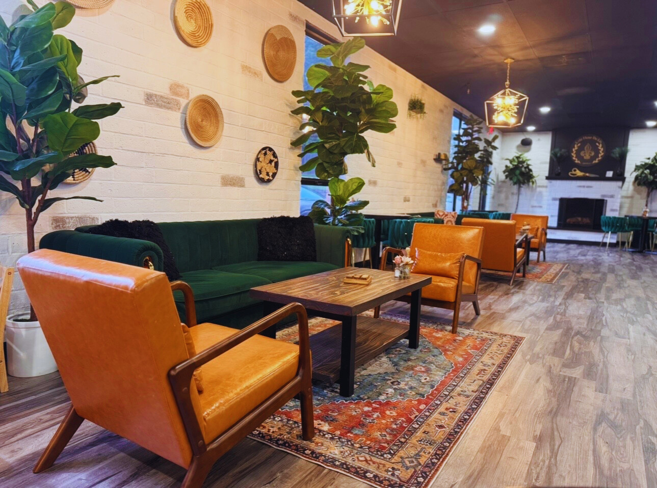 Cozy cafe interior with green and orange seating, potted plants, wall decor, and a fireplace in the background.
