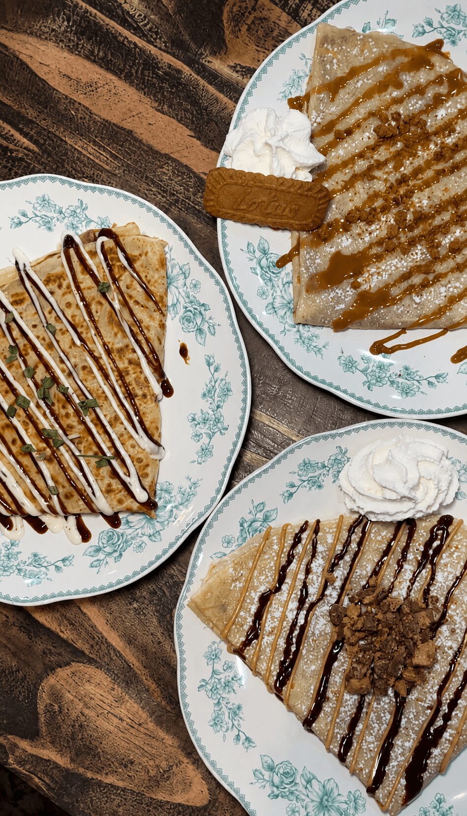 Three plates with slices of cake topped with chocolate drizzle, served with whipped cream and a fork, on a wooden table.