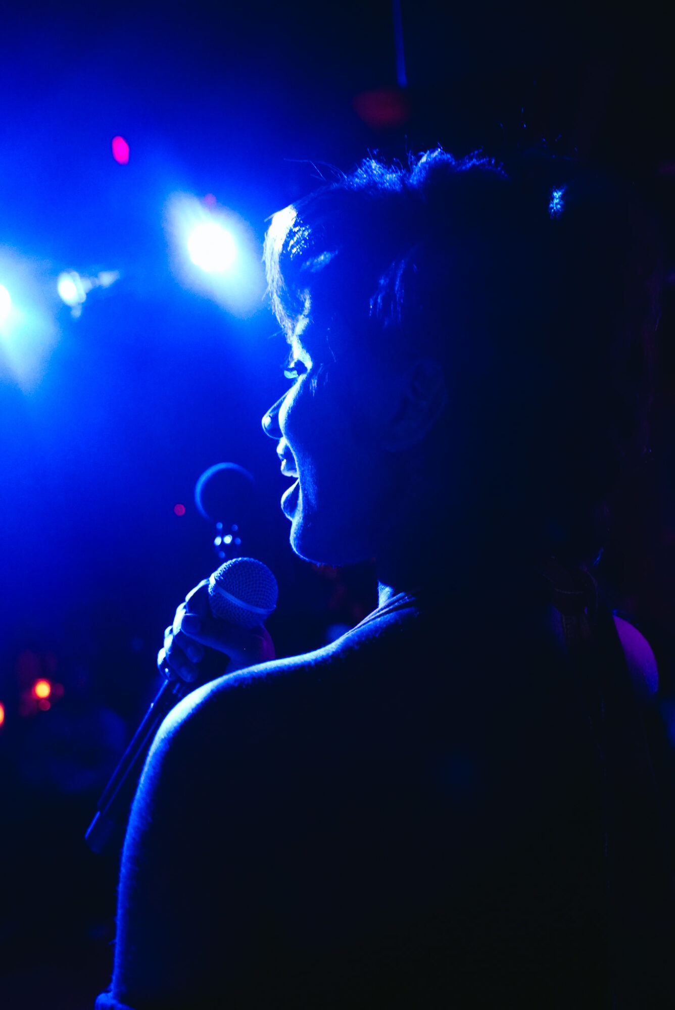 Silhouette of a person holding a microphone on stage with blue and purple lighting.