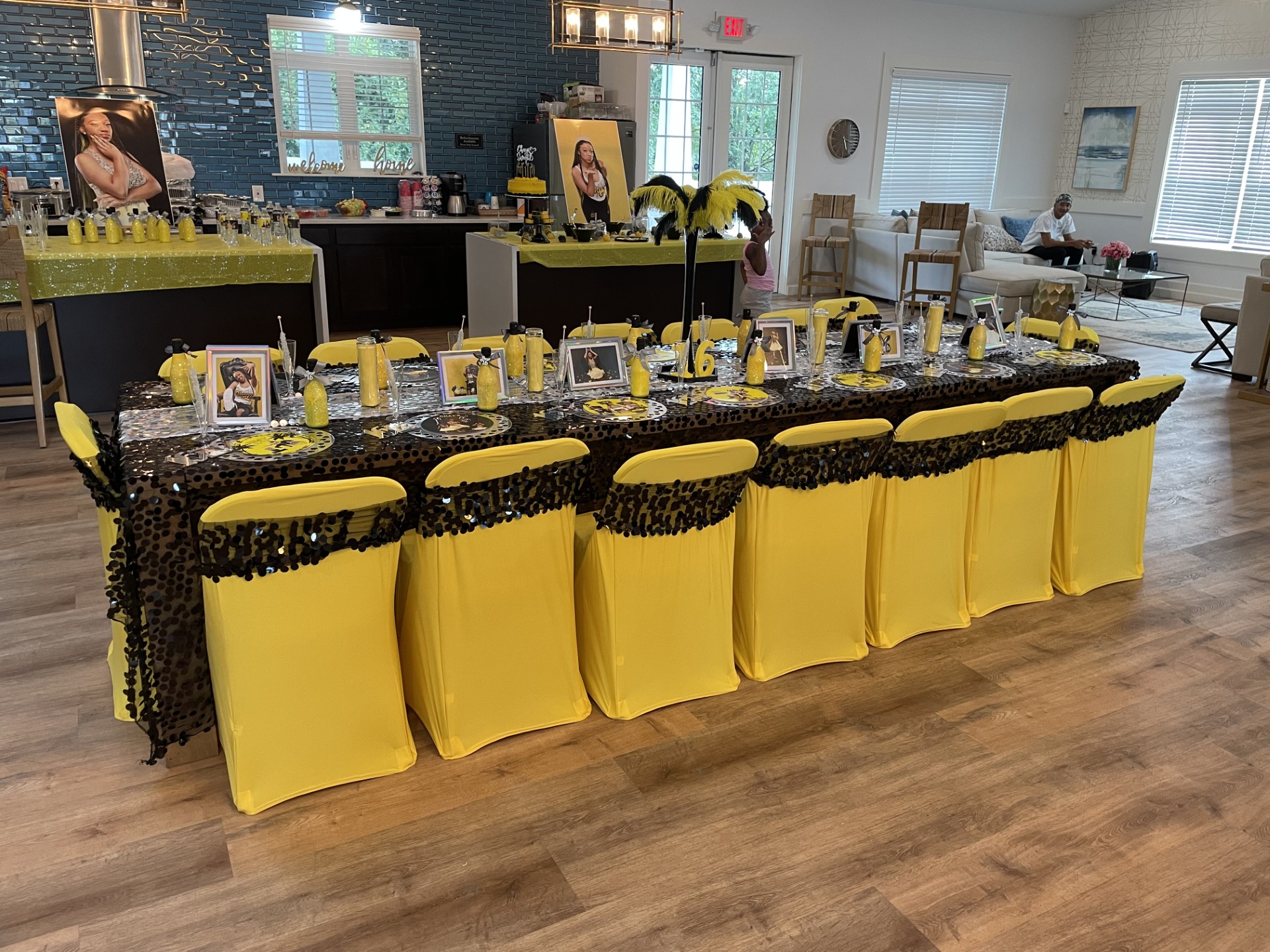 Long table with yellow chairs, black and yellow decorations, and framed photos, set for a celebration in a bright room.