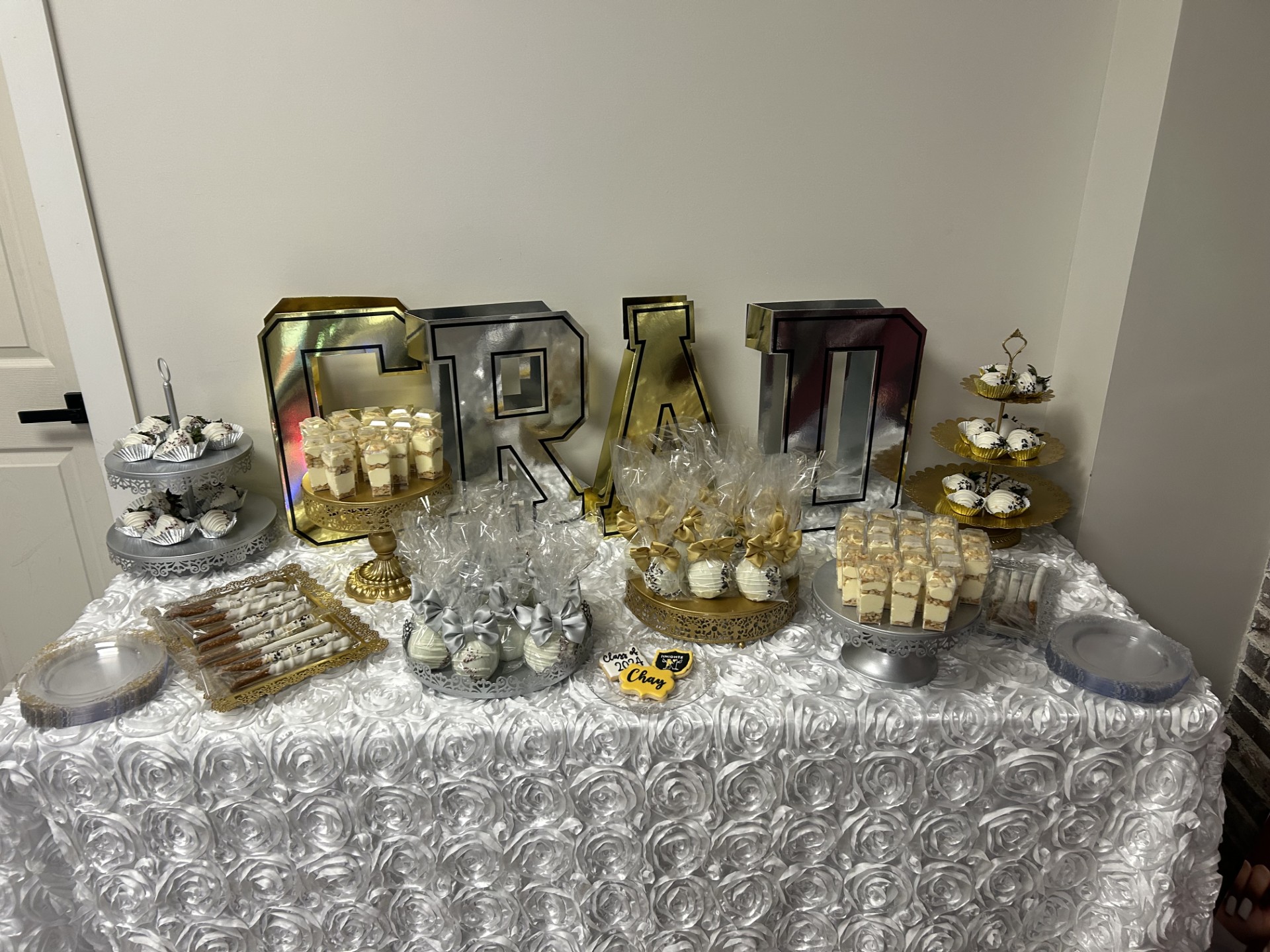Table with silver and gold decorations, cupcakes, and large decorative letters spelling 'GRAD'.