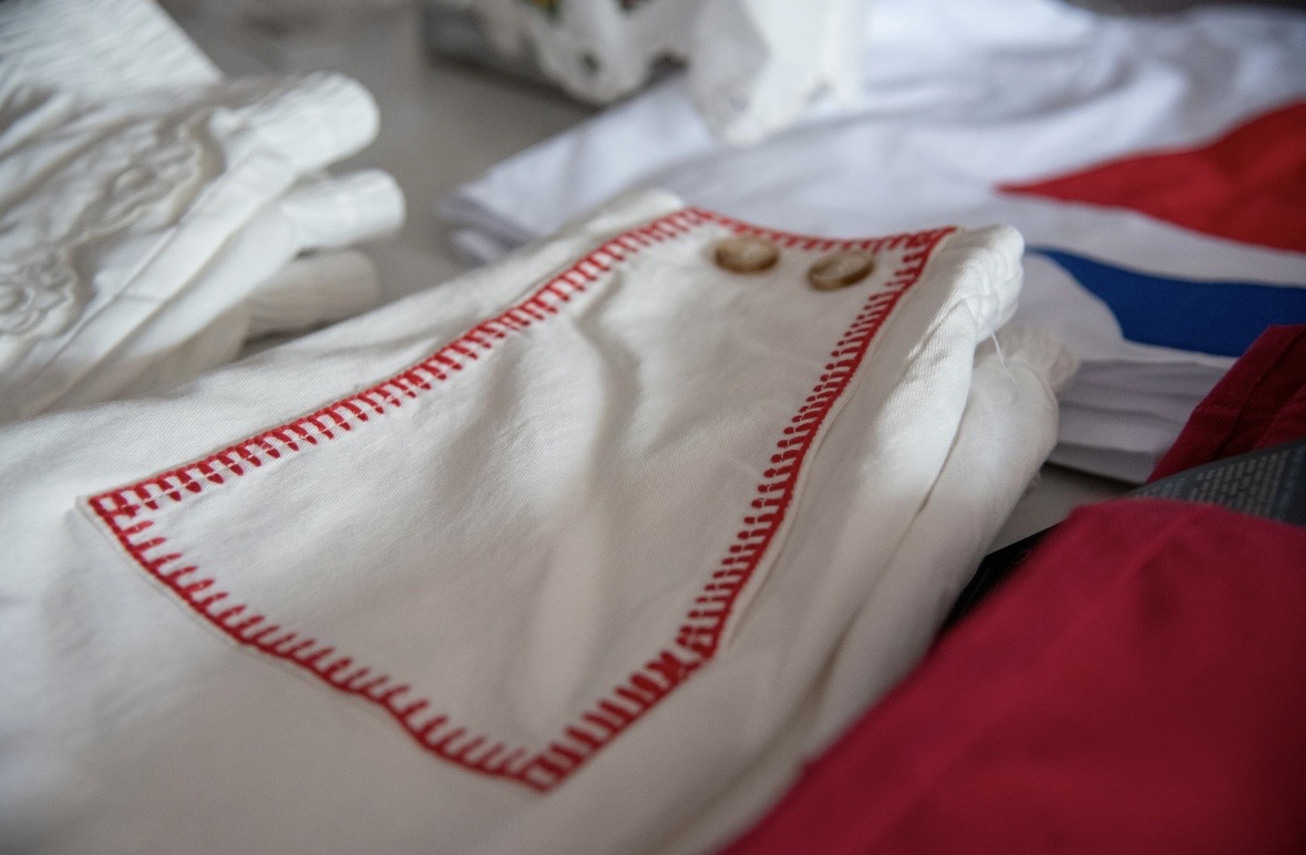 Close-up of a white cloth with red stitching, possibly a handkerchief or napkin, on a bed with other linens.