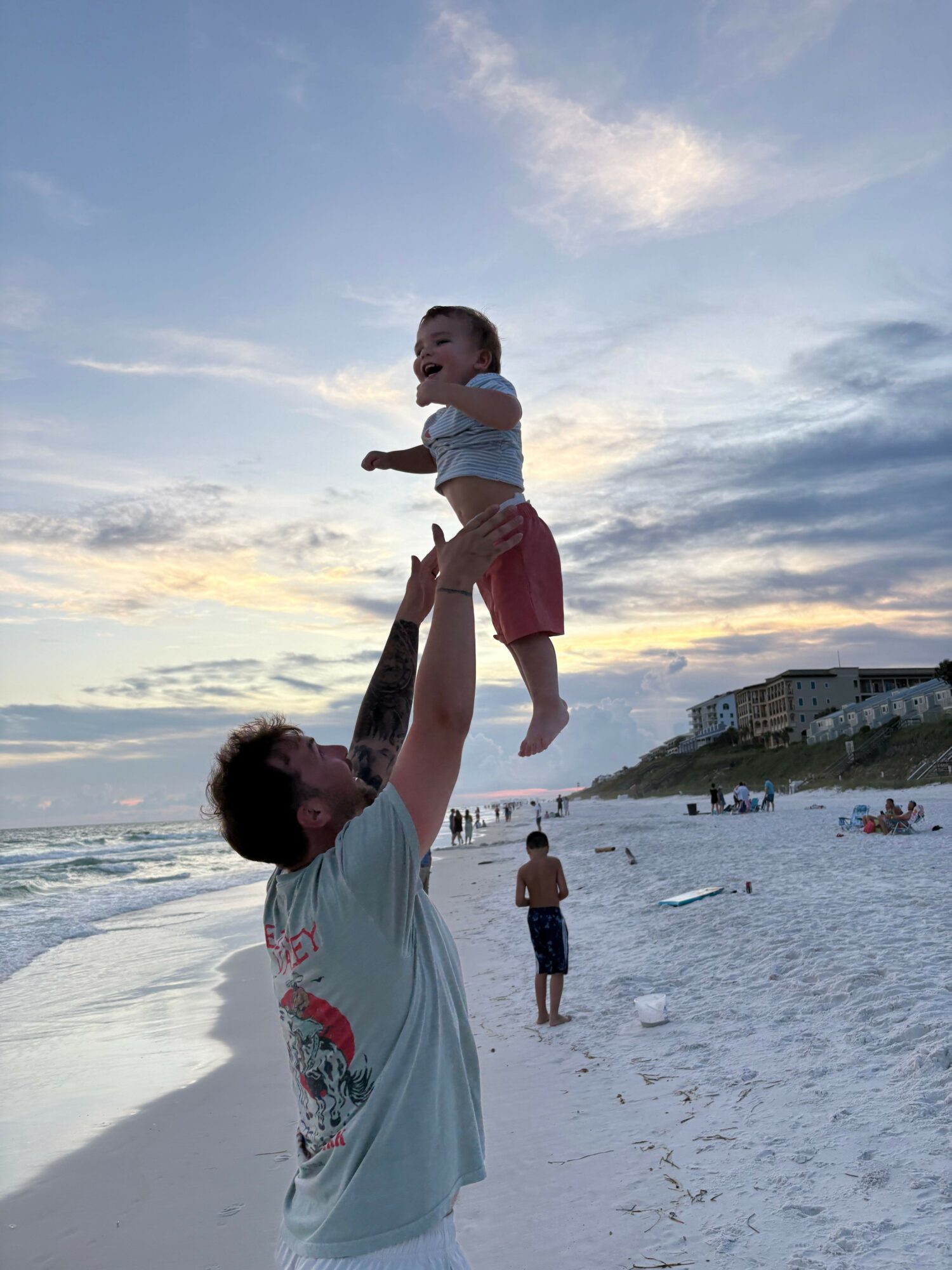 Adult lifting a child on the beach with ocean and sky in background.