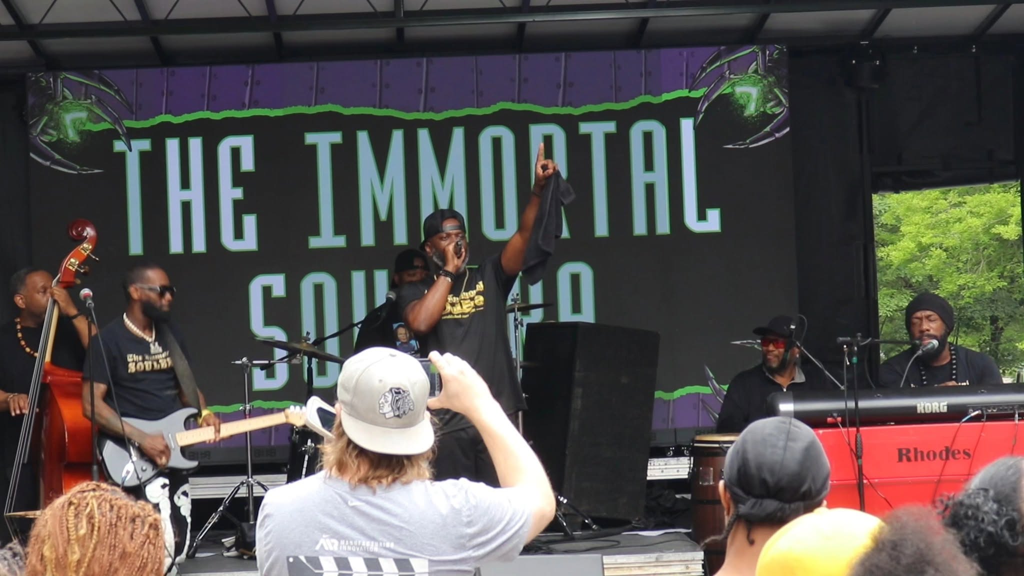 Band performing on stage with a large screen behind them displaying 'THE IMMORTAL SOUL' at an outdoor event.