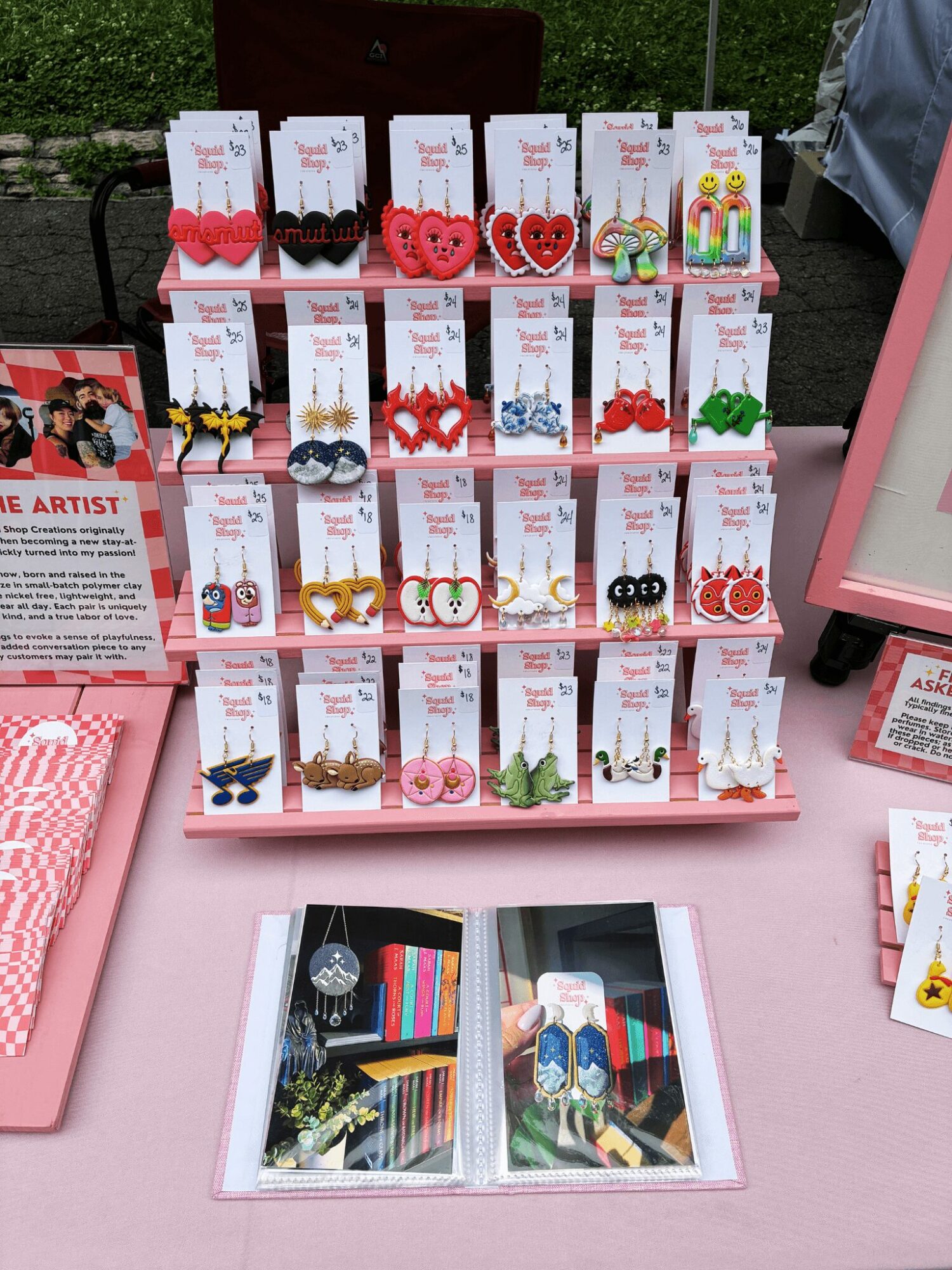 Display of colorful earrings on cards arranged on a pink table, with a photo album open in front.