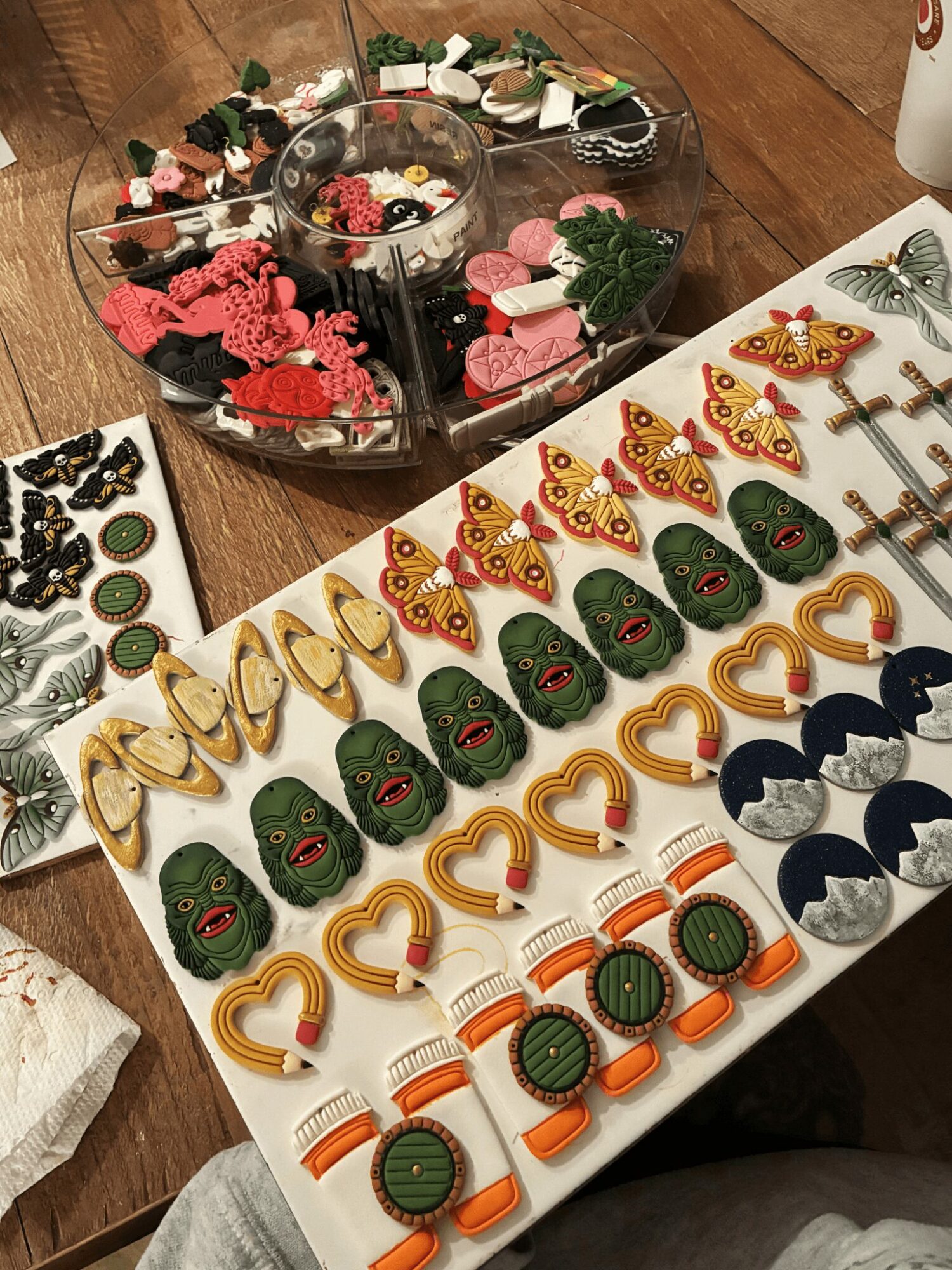 Assorted colorful earrings and jewelry displayed on a white tray, with a container of decorative items in the background.