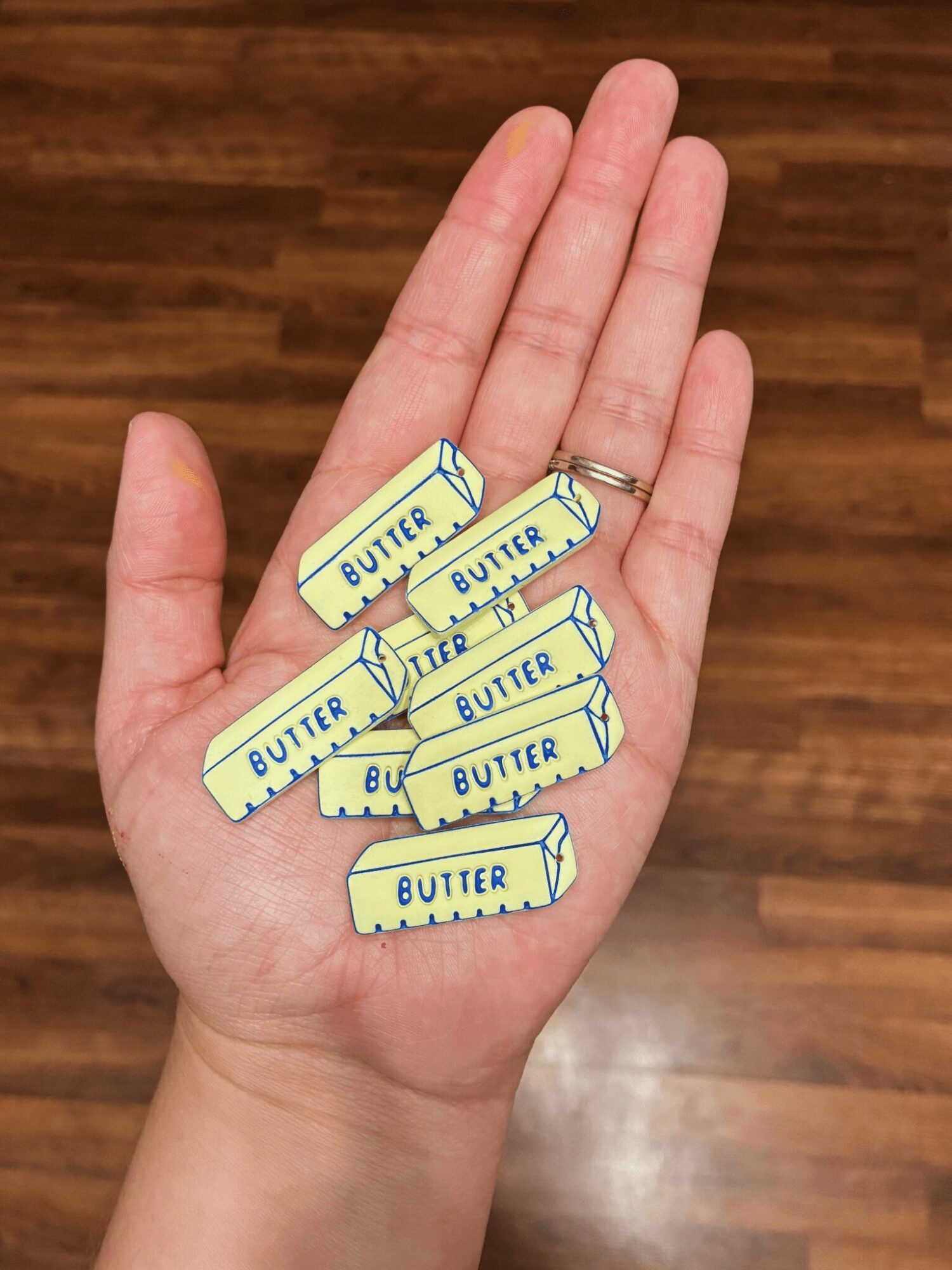 Hand with seven butter-shaped erasers on fingers, background of wooden floor, clear and well-lit.