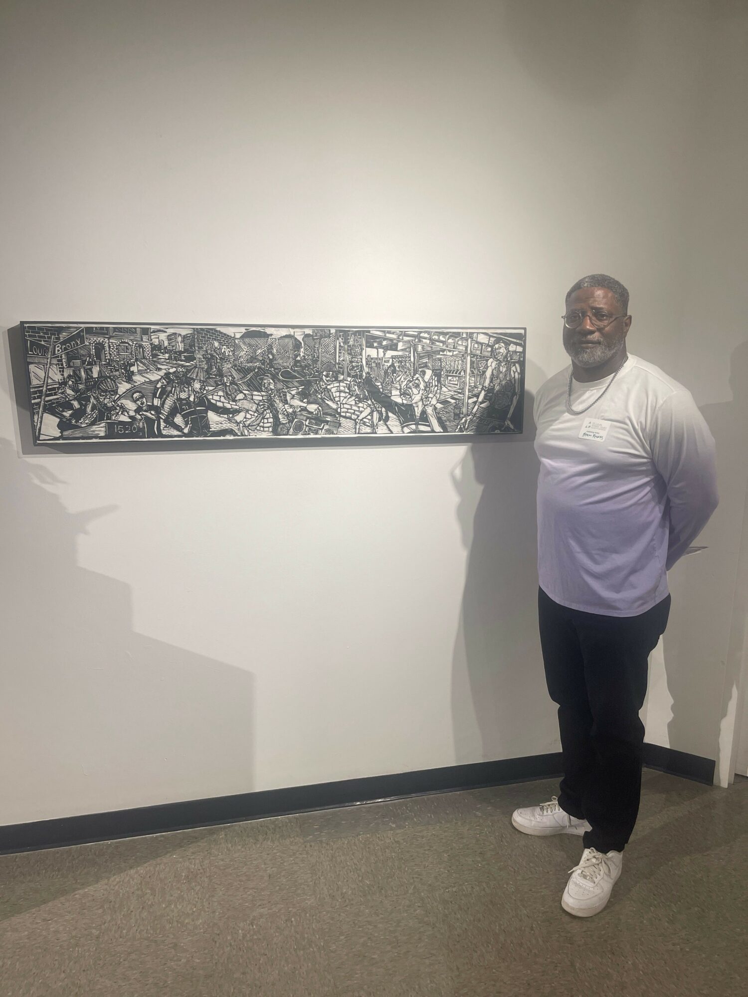 Man standing next to a panoramic black-and-white cityscape photograph on a white wall.