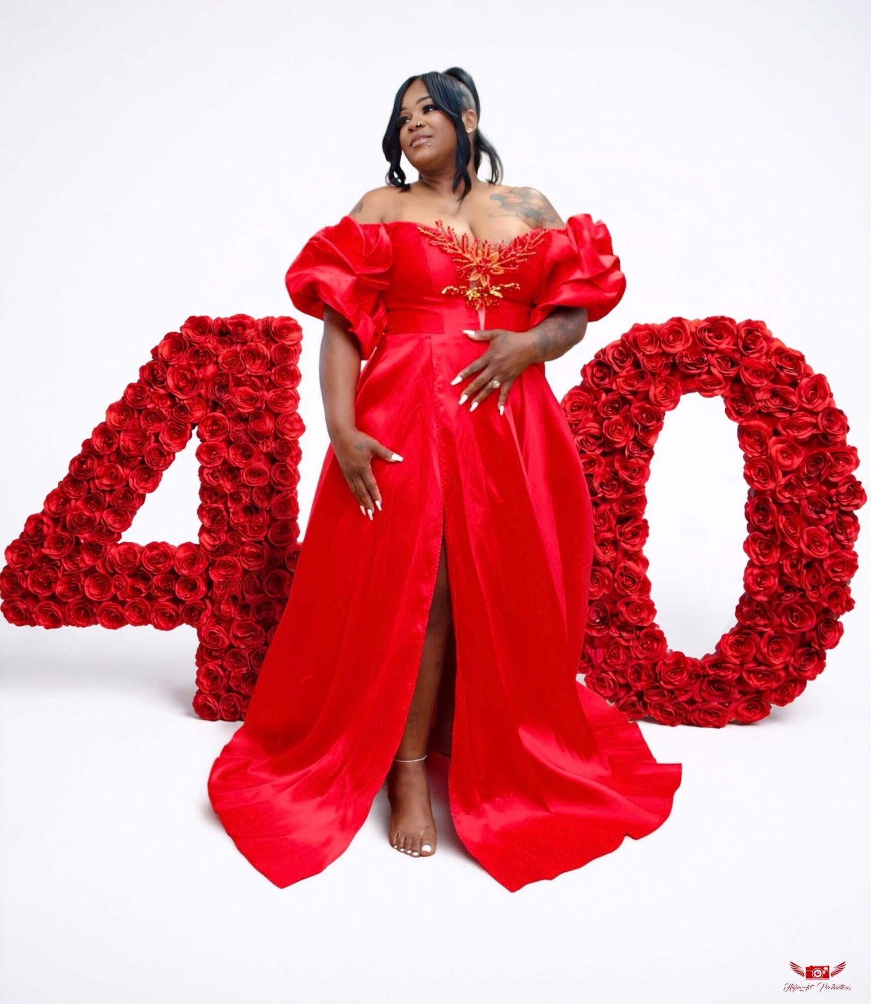 Woman in a red gown standing in front of large number 40 made of red flowers, against a white background.