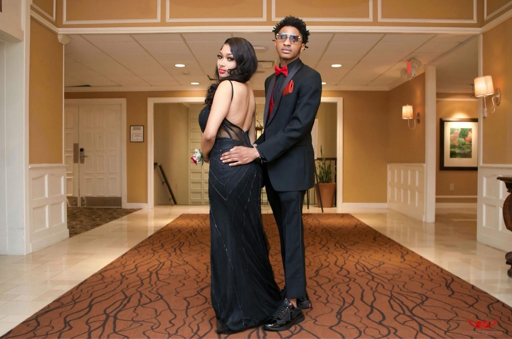 A man and woman in formal attire standing in a hotel lobby with warm lighting and artwork on the walls.