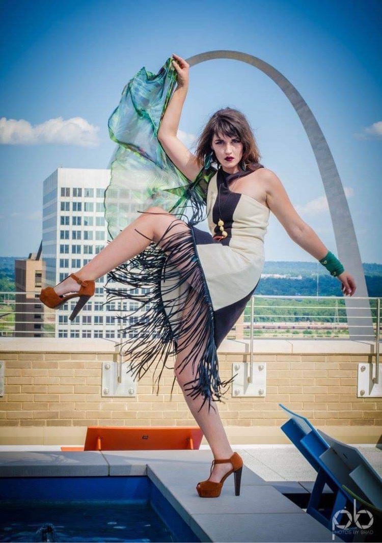 Woman in a dress and high heels poses on a rooftop with cityscape and the Gateway Arch in background.