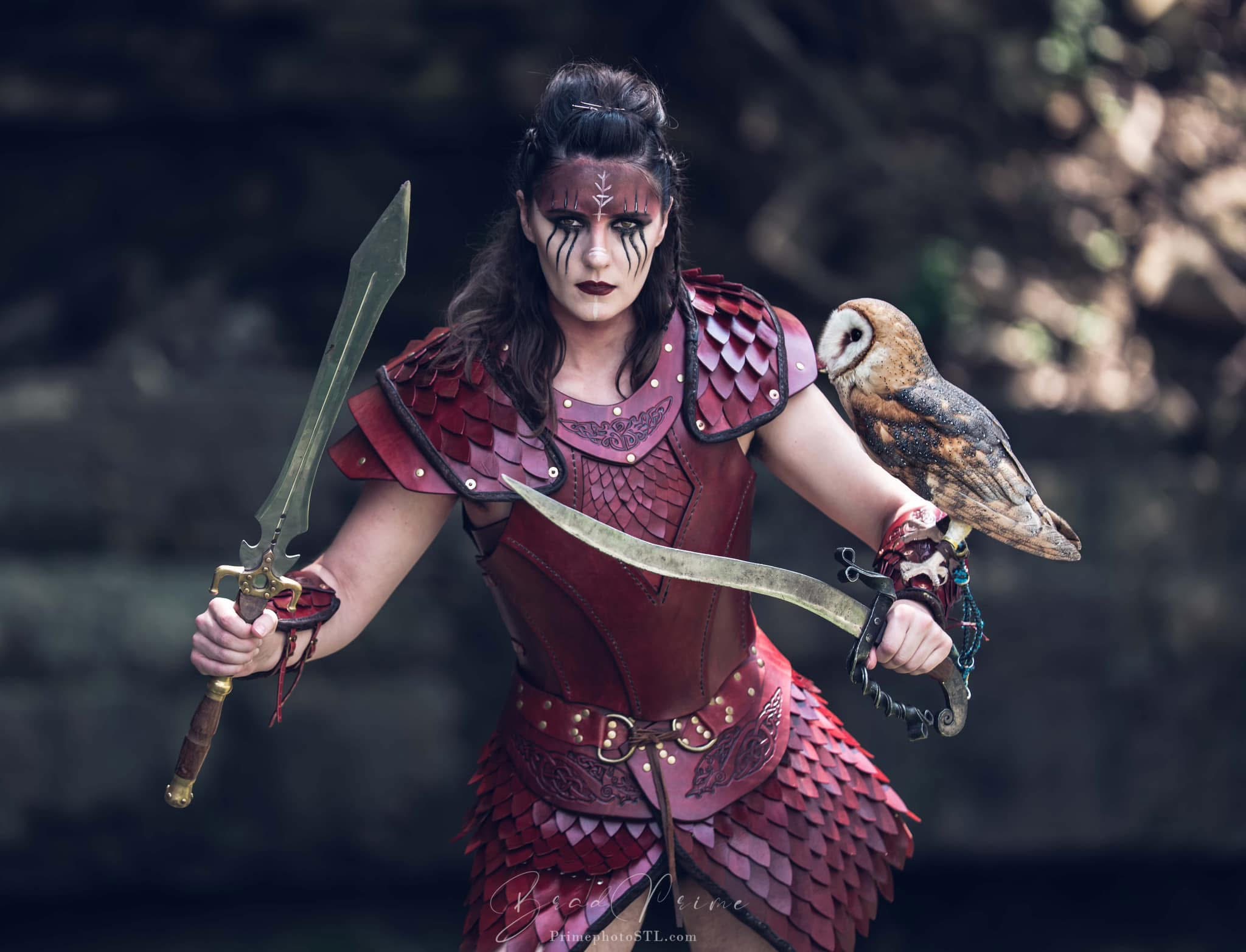 Person dressed as a fantasy warrior with face paint, holding a sword and an owl on their arm outdoors.