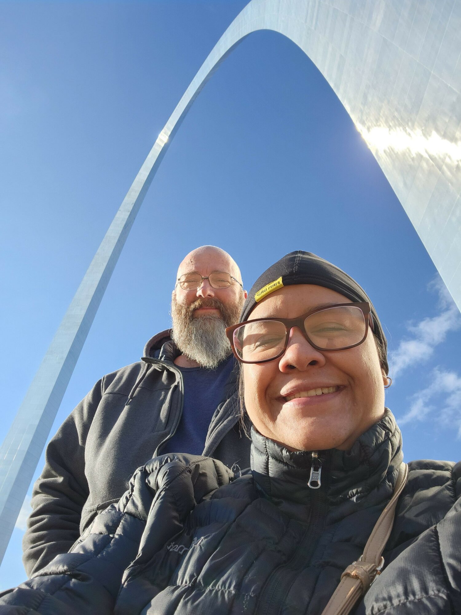 Two people smiling outdoors with a blue sky and water in the background.