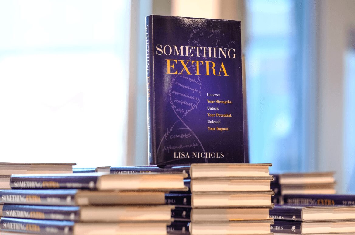 Stack of books with a prominent book titled 'Something Extra' by Lisa Nichols in the background.