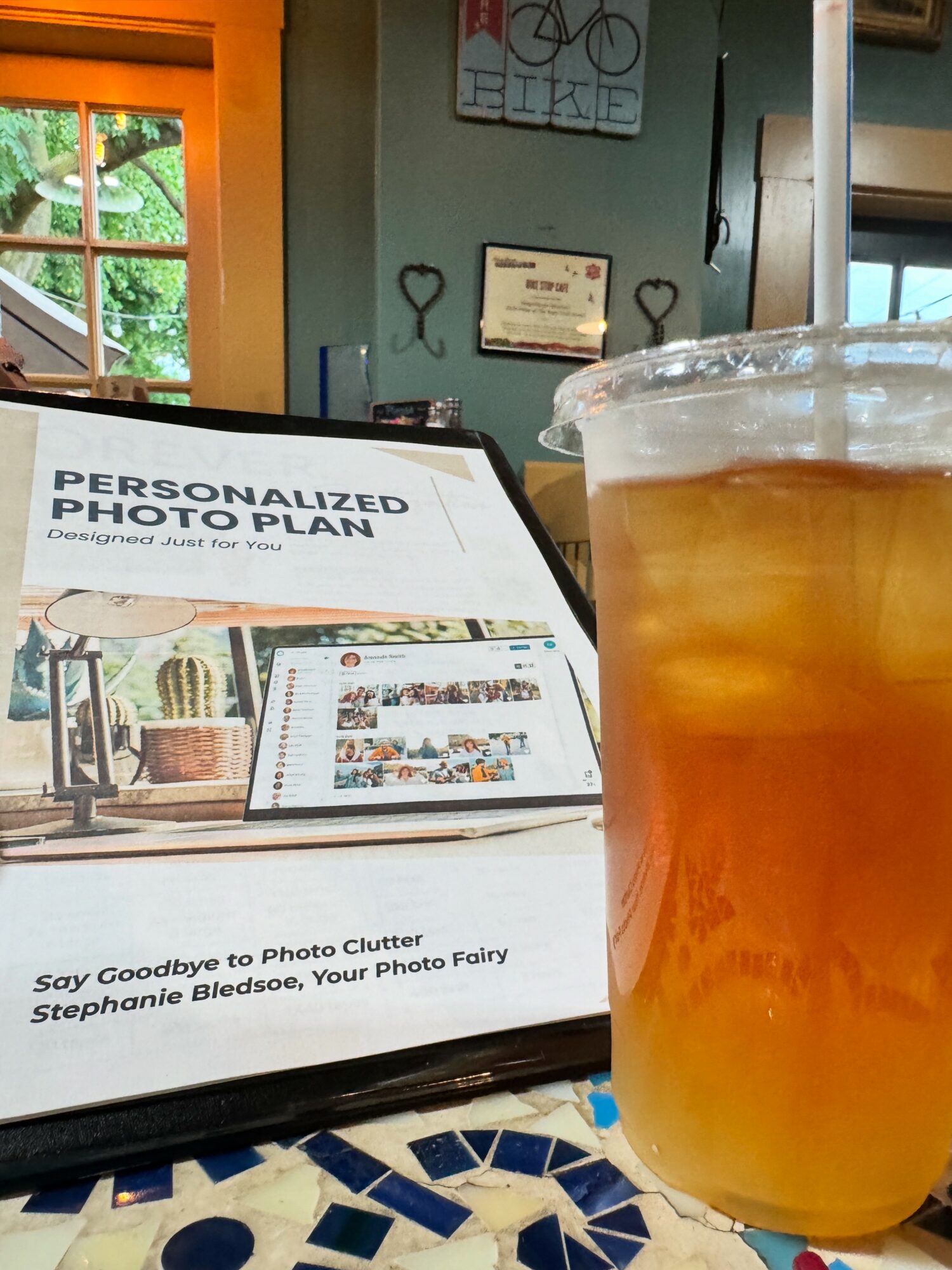 A glass of beer on a table with a personalized photo plan display in the foreground, background shows a window and wall decor.