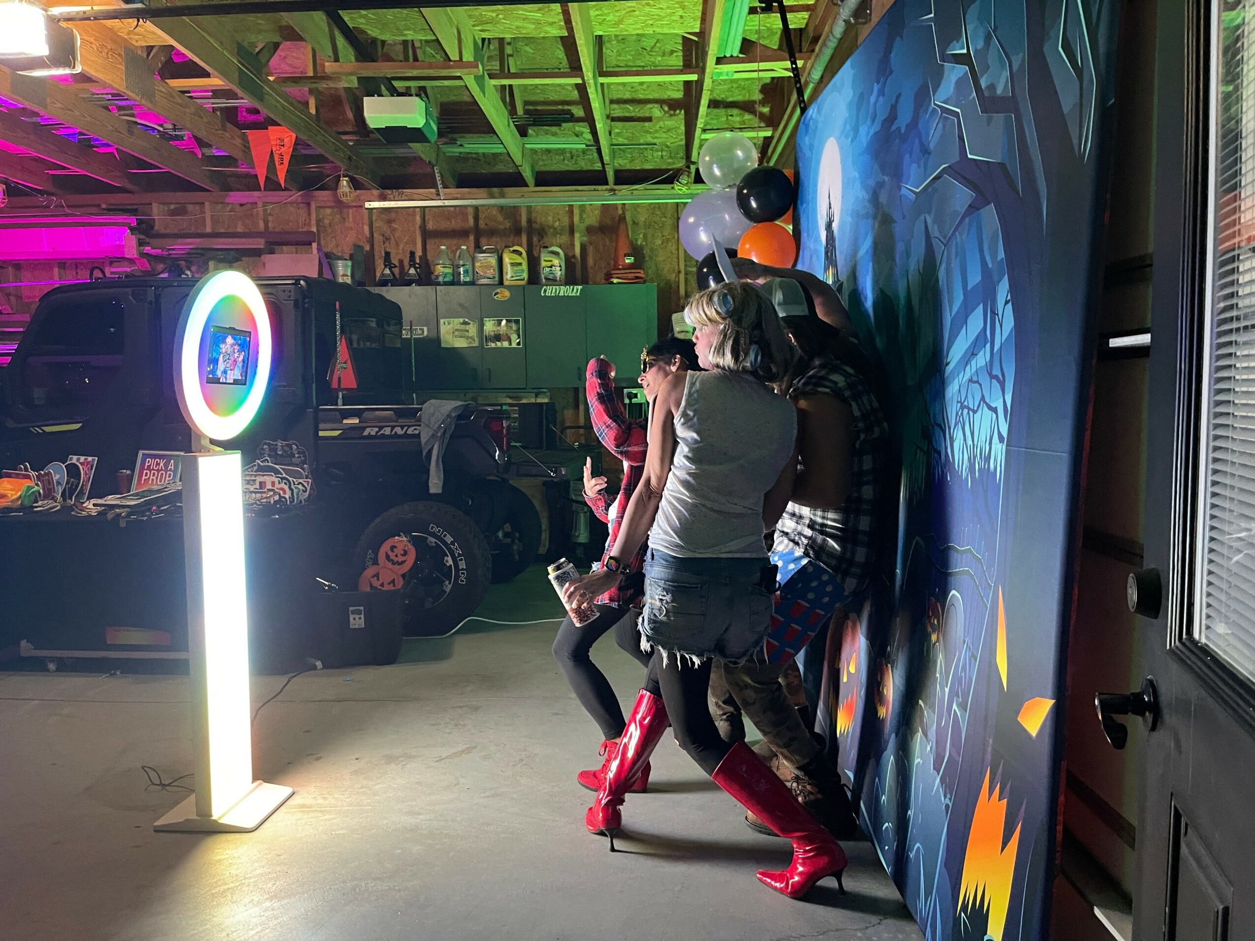 Two women dance in an arcade with colorful lighting and a wall mural, wearing casual clothes and red boots.