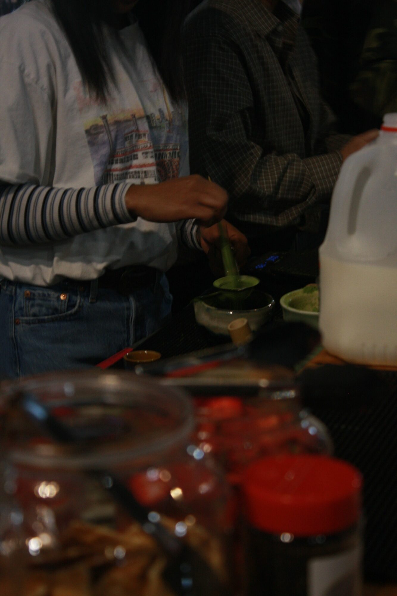 People sitting at a table with drinks and food, some holding glasses, in a dimly lit setting.