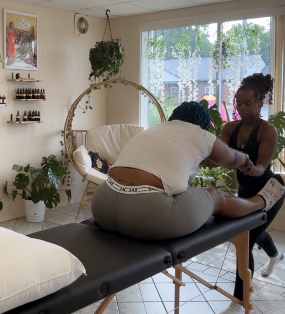 Person receiving a massage on a massage table in a bright room with plants and large window.