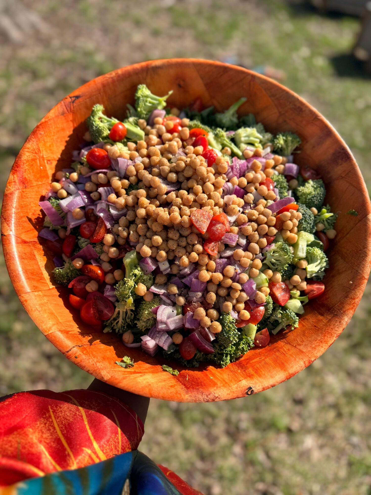 Bowl of mixed salad with lentils, broccoli, red onion, and cherry tomatoes outdoors.