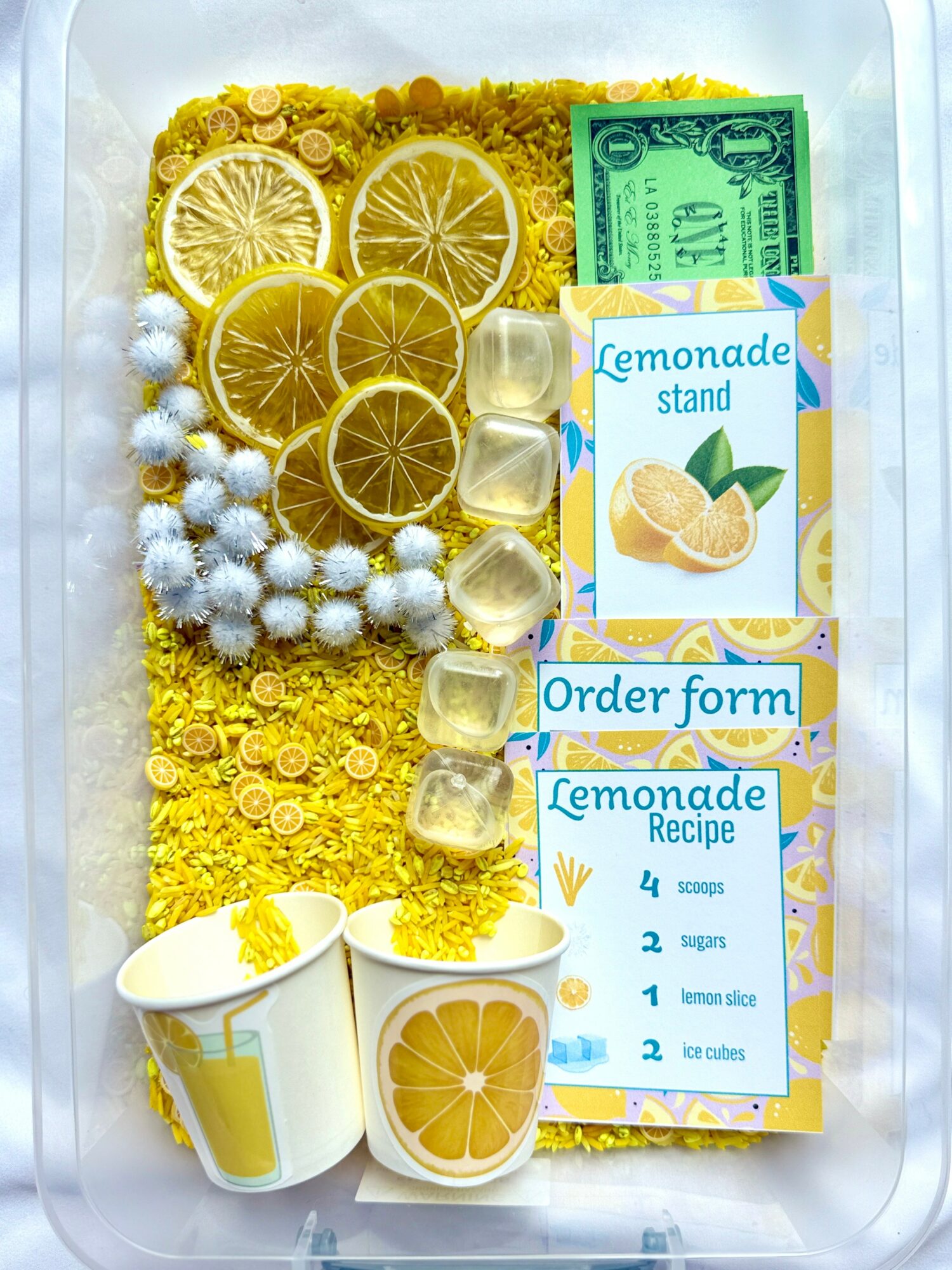 Lemon slices, white flowers, a dollar bill, lemonade stand sign, order form, and cups with lemon images on a yellow background.
