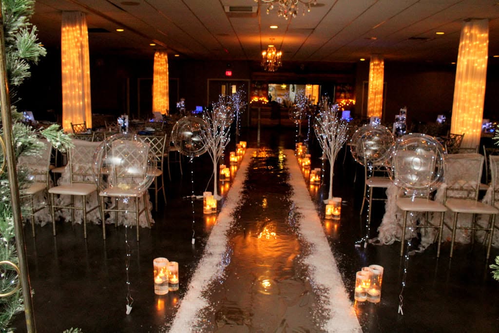 Elegant event space with a reflective aisle, decorated tables, candles, and warm lighting, ready for a celebration.