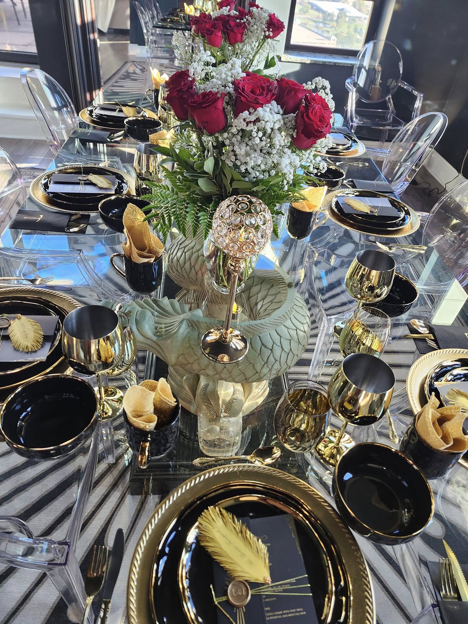 Elegant table setting with black and gold plates, gold utensils, and a floral centerpiece of pink and white flowers.