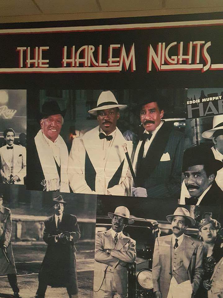 Group of men in vintage suits and hats, with a sign reading 'The Harlem Nights' above them.