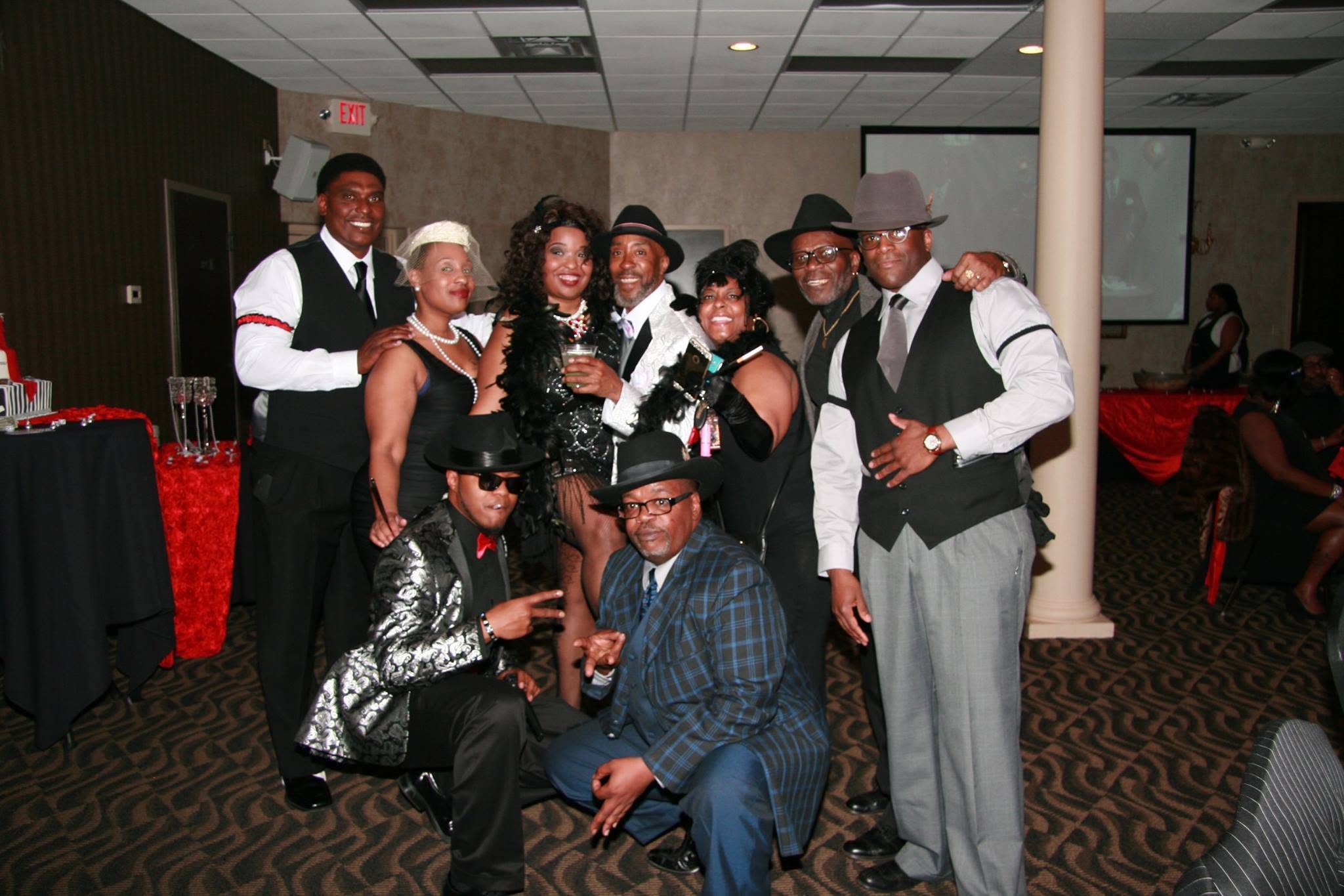 Group of nine people dressed in formal attire, smiling and posing together indoors at a celebration.