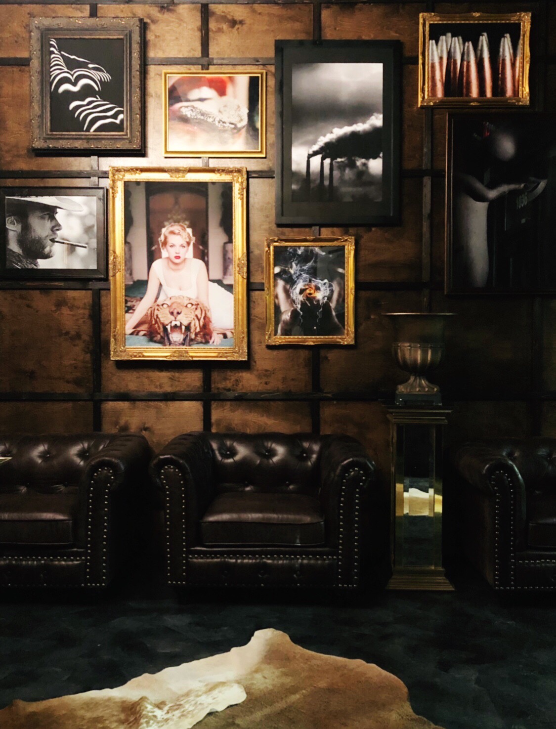 Wall decorated with framed pictures, including a child, landscape, and abstract images, above leather sofas and a side table.