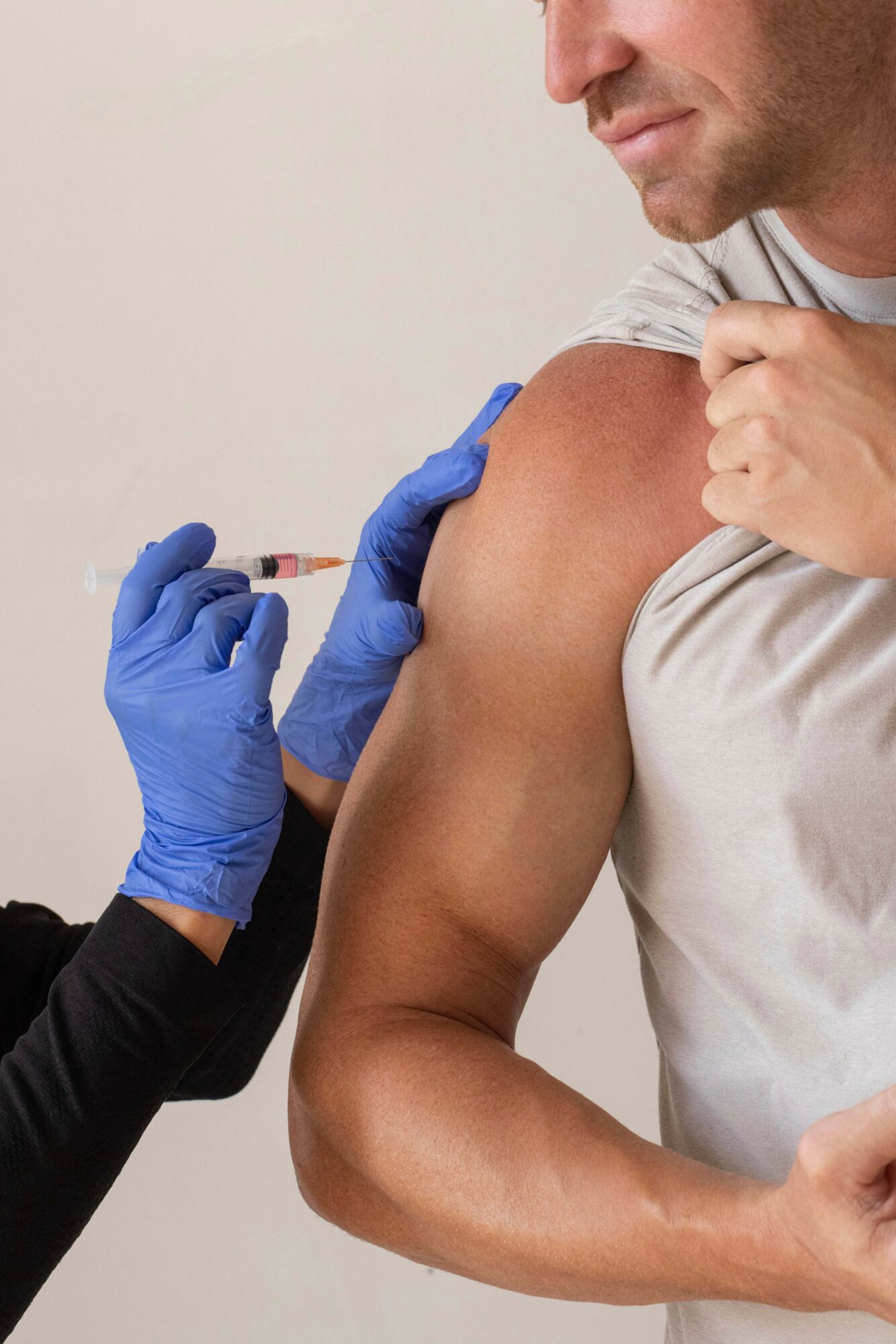 Person receiving a vaccination in upper arm from healthcare worker wearing blue gloves, close-up view.
