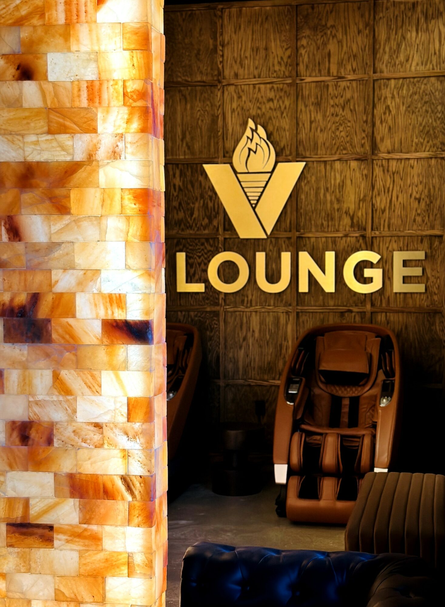 Interior lounge with a wooden wall, illuminated salt wall, and massage chairs, with a lounge sign and logo on the wall.