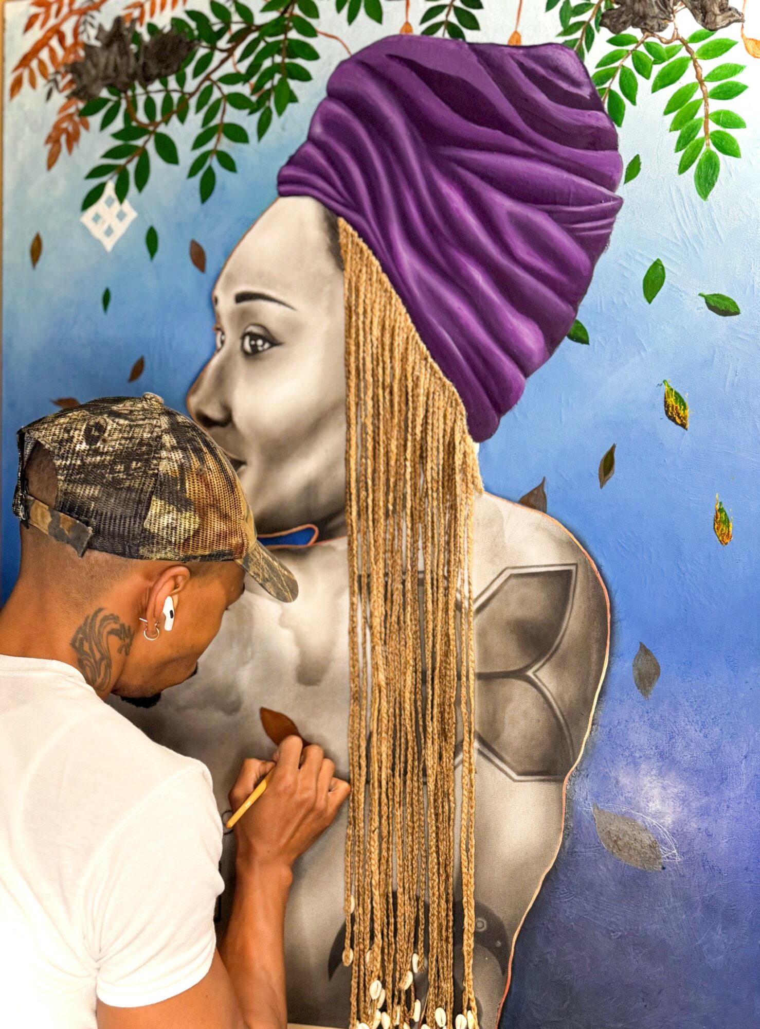 Person with a purple headwrap and long blonde braids faces a painted bust sculpture, with green leaves in the background.