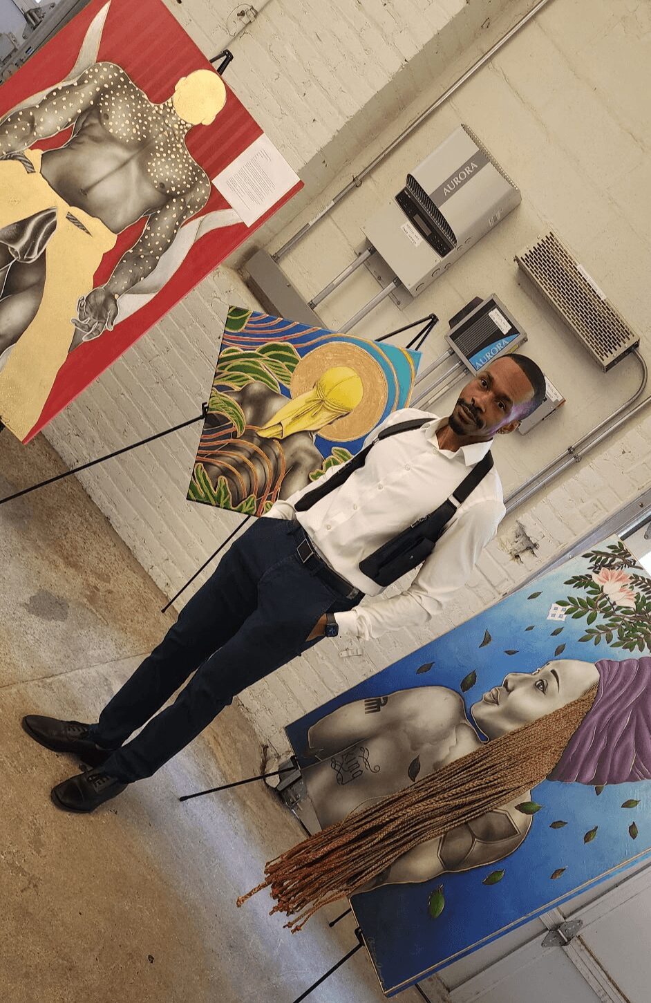 Person taking a selfie in front of colorful paintings, wearing glasses, a white shirt, and a black tie, with art displayed behind.