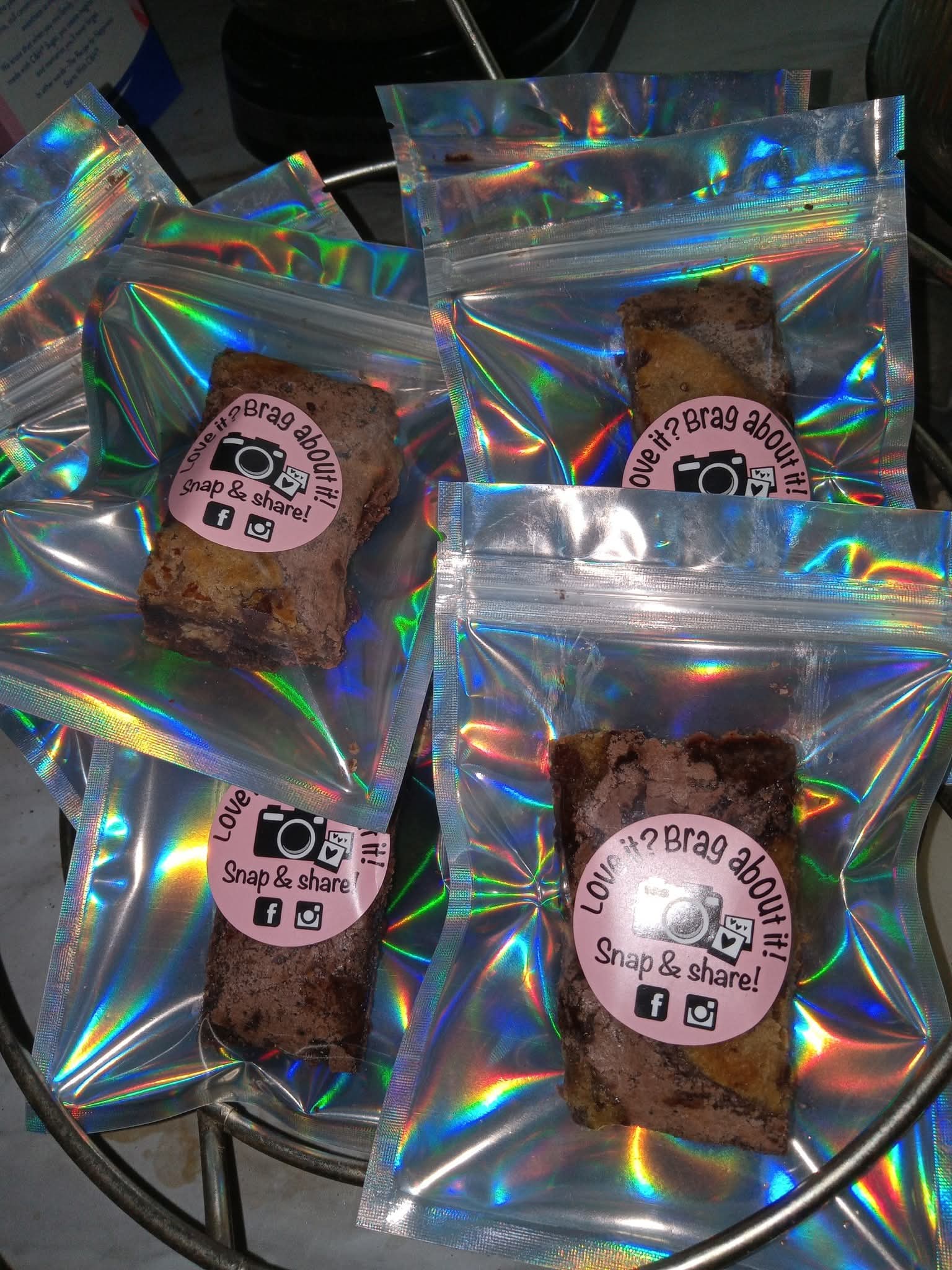 Four holographic bags with cookies inside, each bag has a pink label with text and a small car icon.