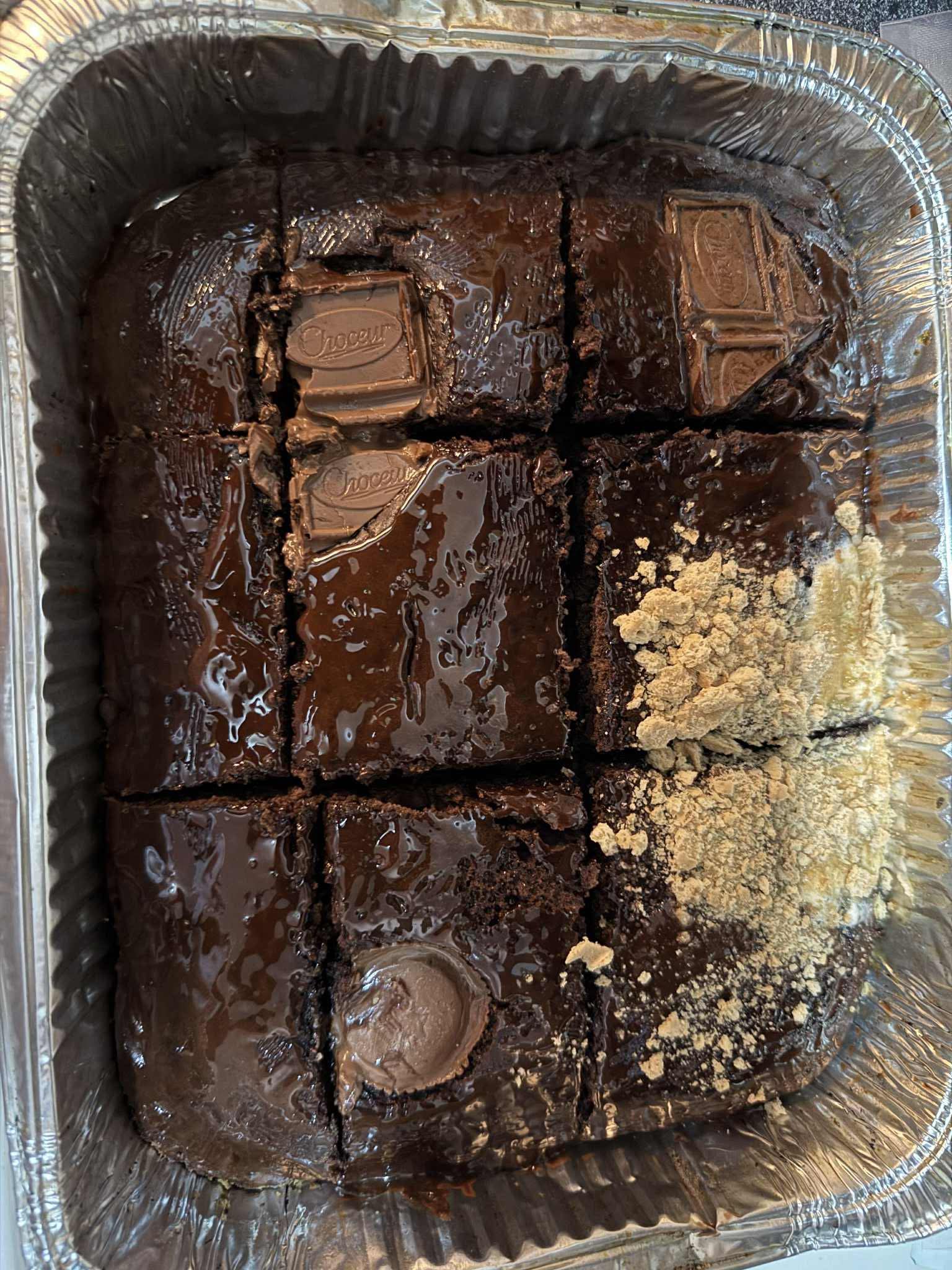 Six chocolate brownies in a tray, some with chocolate topping, one with crumbled topping, all cut into squares.