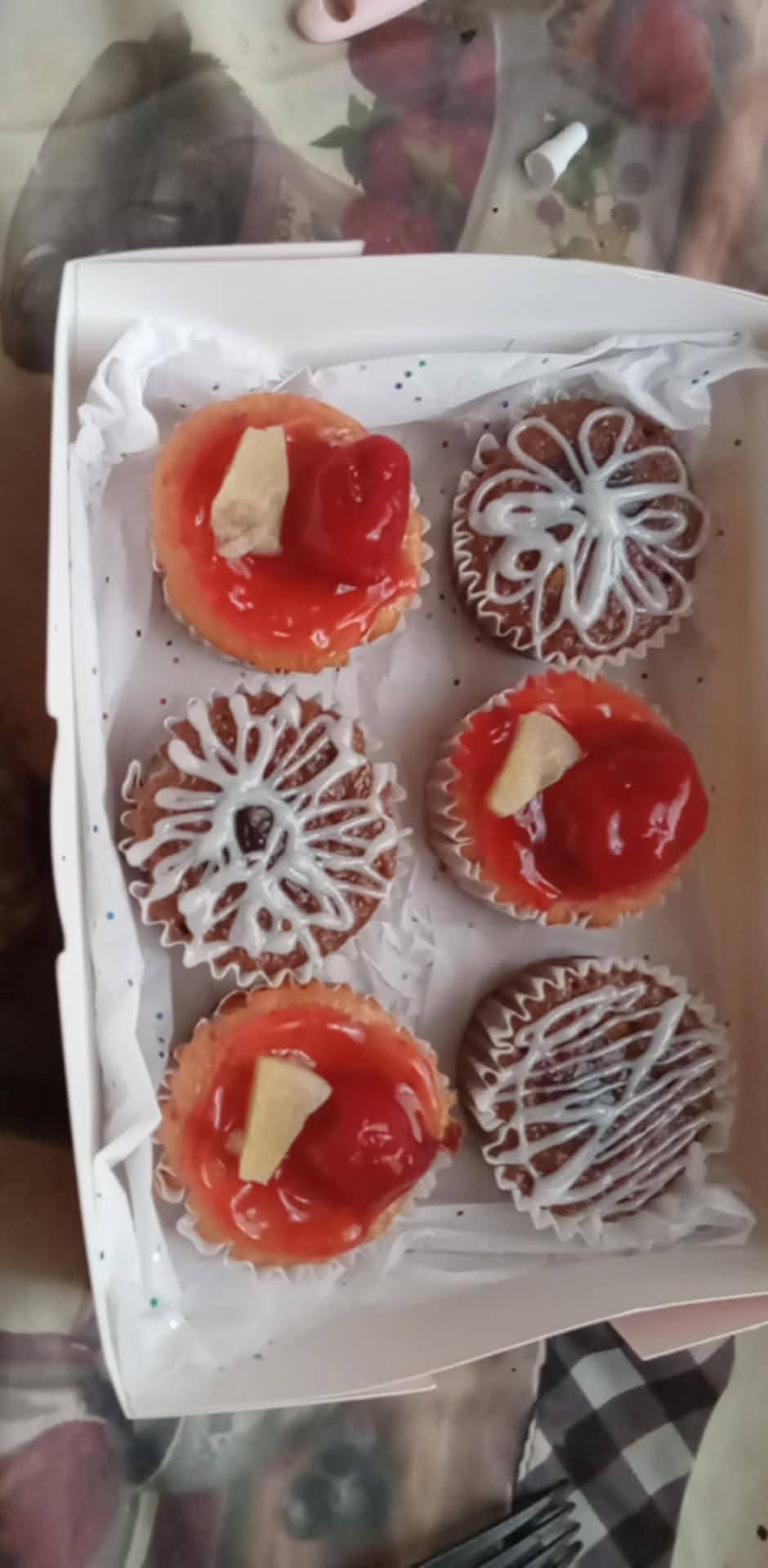 Six cupcakes with red icing, white chocolate pieces, and decorative white icing patterns on a white tray.