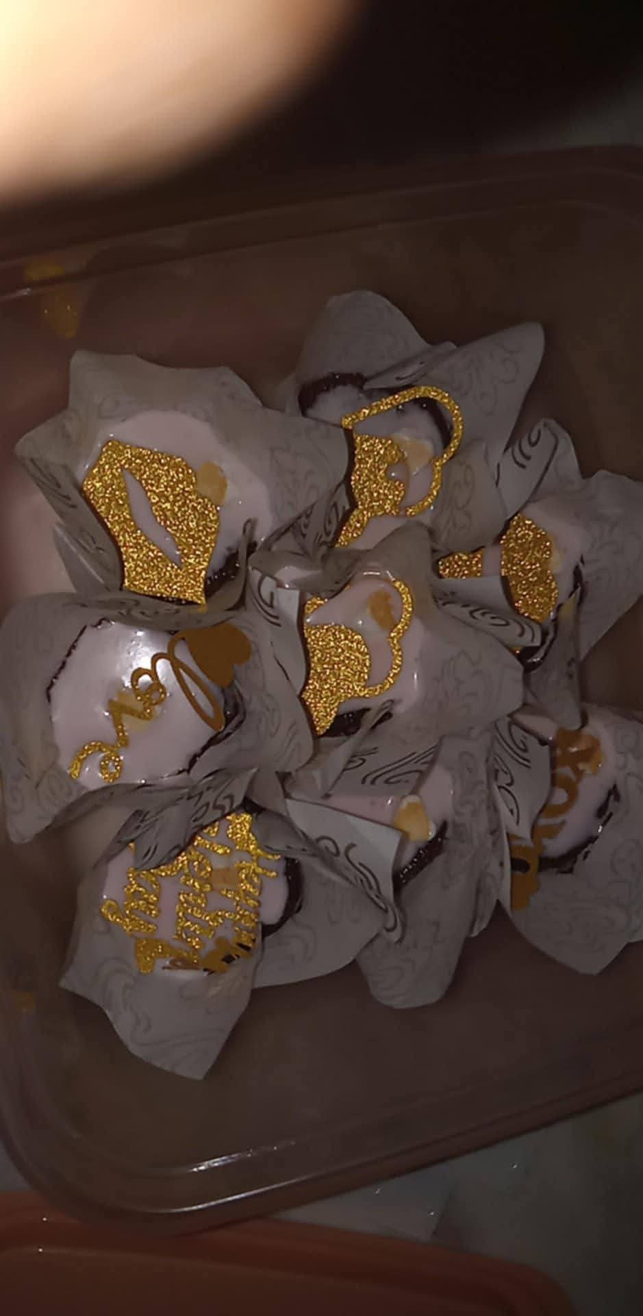 Multiple small candies wrapped in white paper with gold designs inside a container.