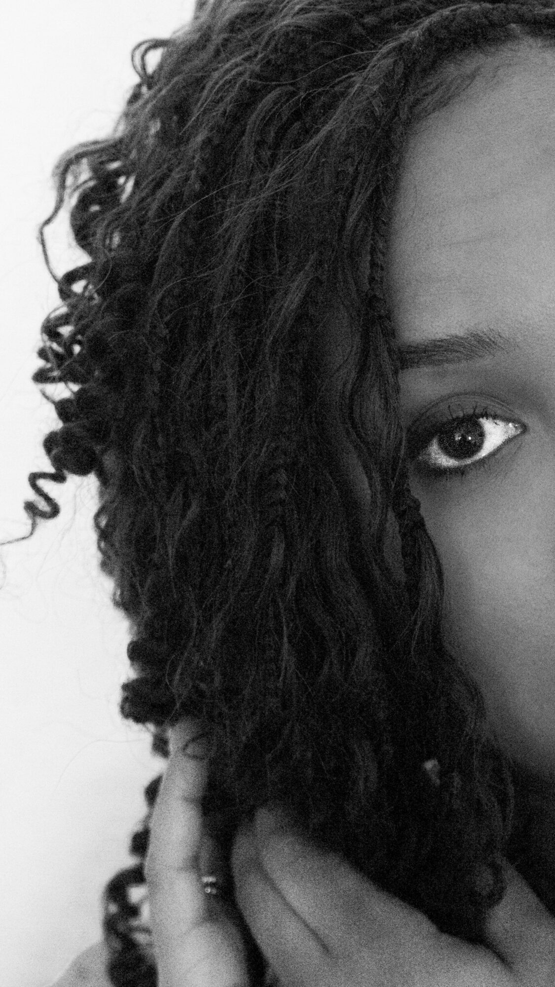 Close-up of a person's face with curly hair covering part of it, focusing on one eye and hand.