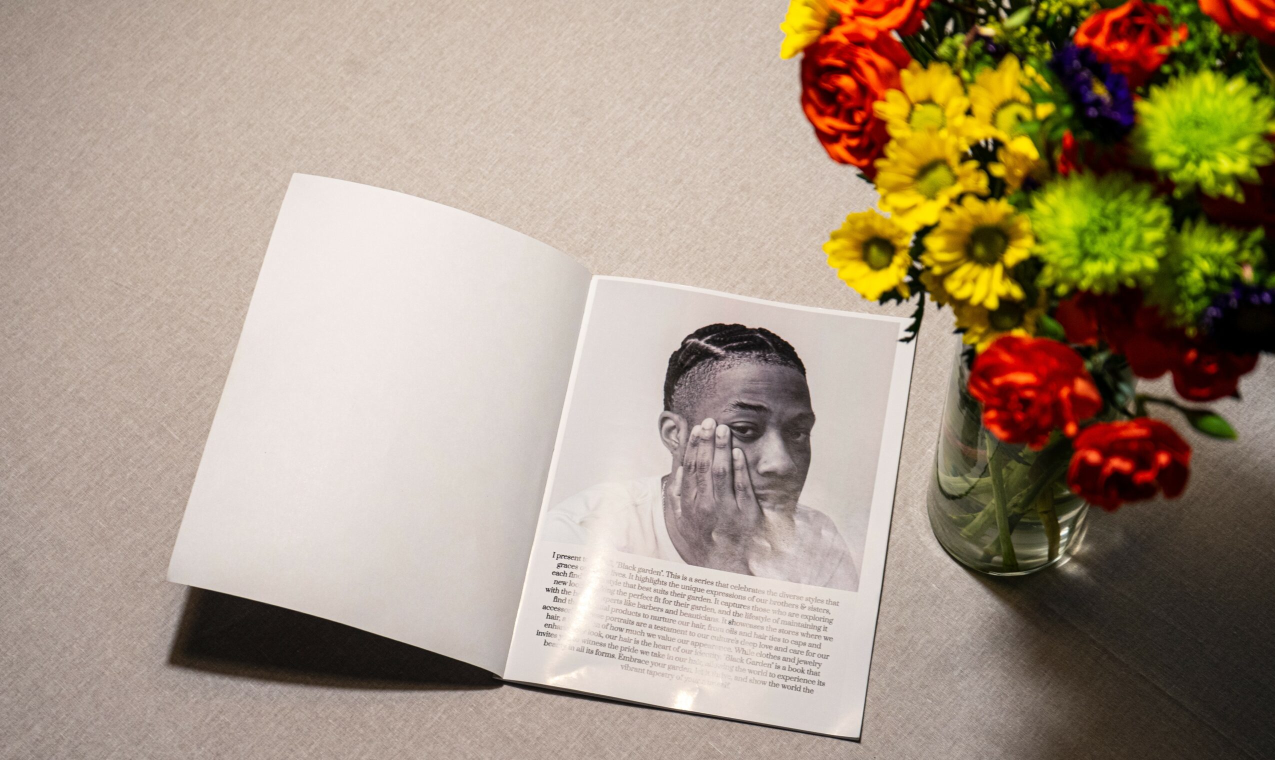 Open magazine with a black-and-white portrait of a person, next to a colorful flower arrangement in a glass vase on a beige surface.