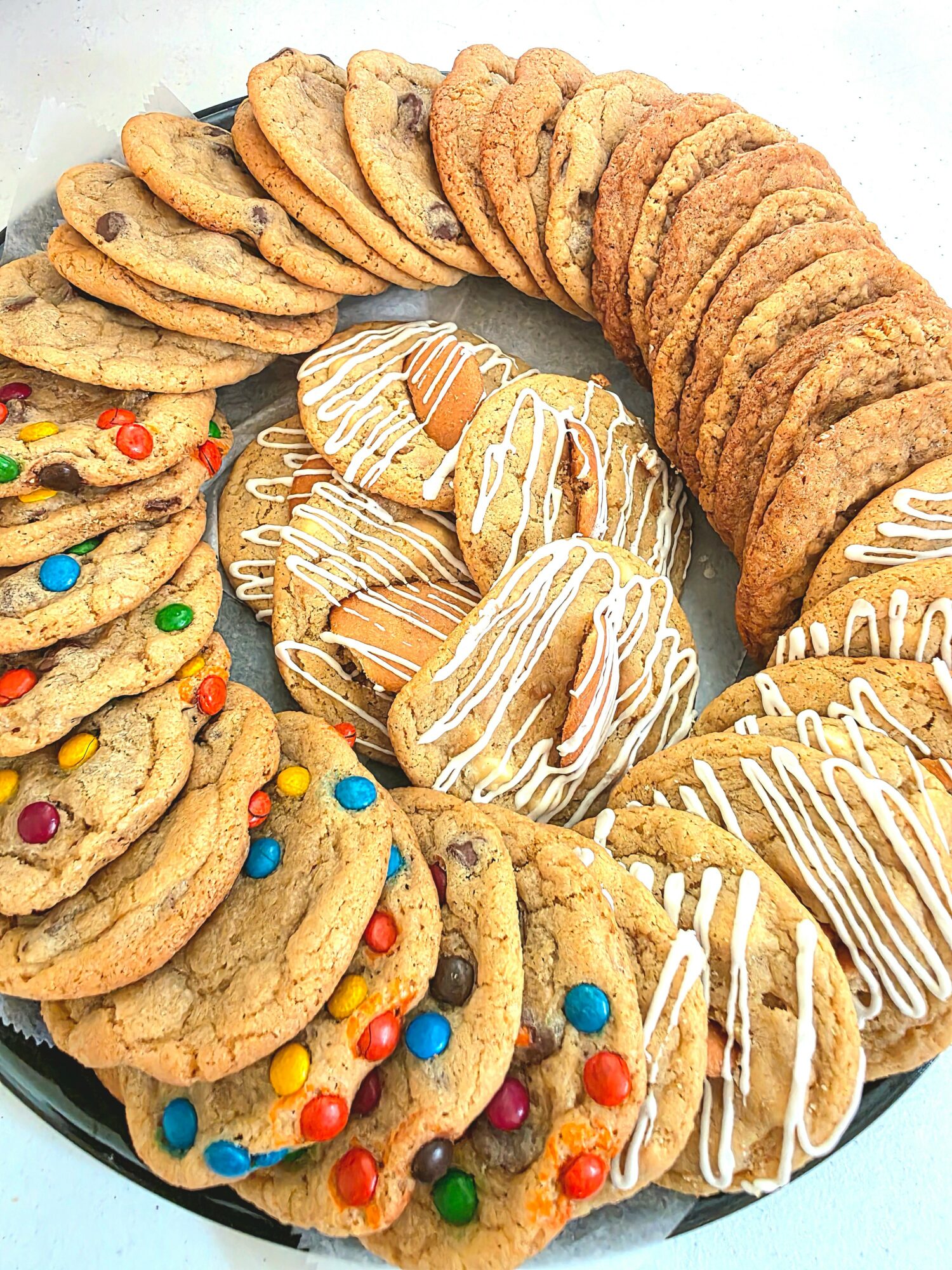 Assorted cookies arranged in a circular pattern on a plate, including decorated cookies with colorful candies and drizzled cookies.