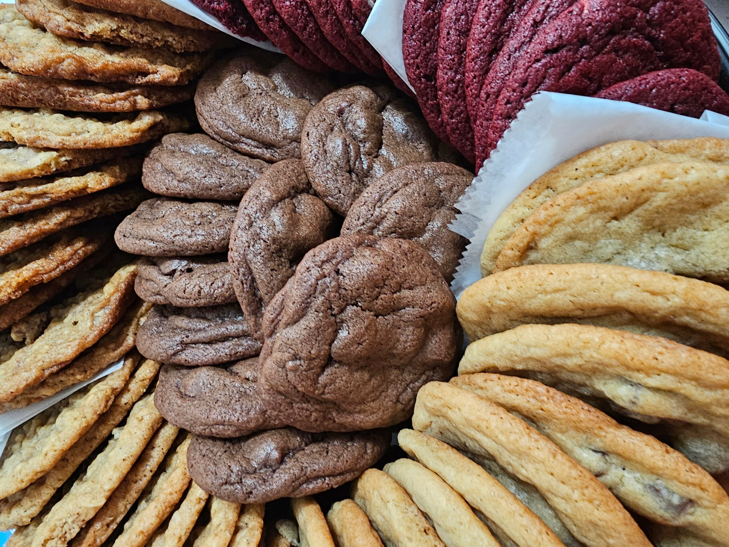Assorted cookies and baked goods arranged in a display, including chocolate chip, sugar, and red velvet cookies.