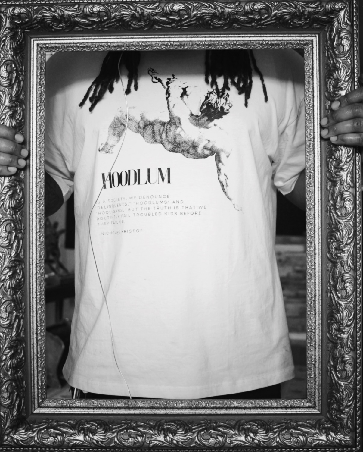 Person holding a decorative frame, wearing a T-shirt with text and graphic design, with hands visible on sides of the frame.