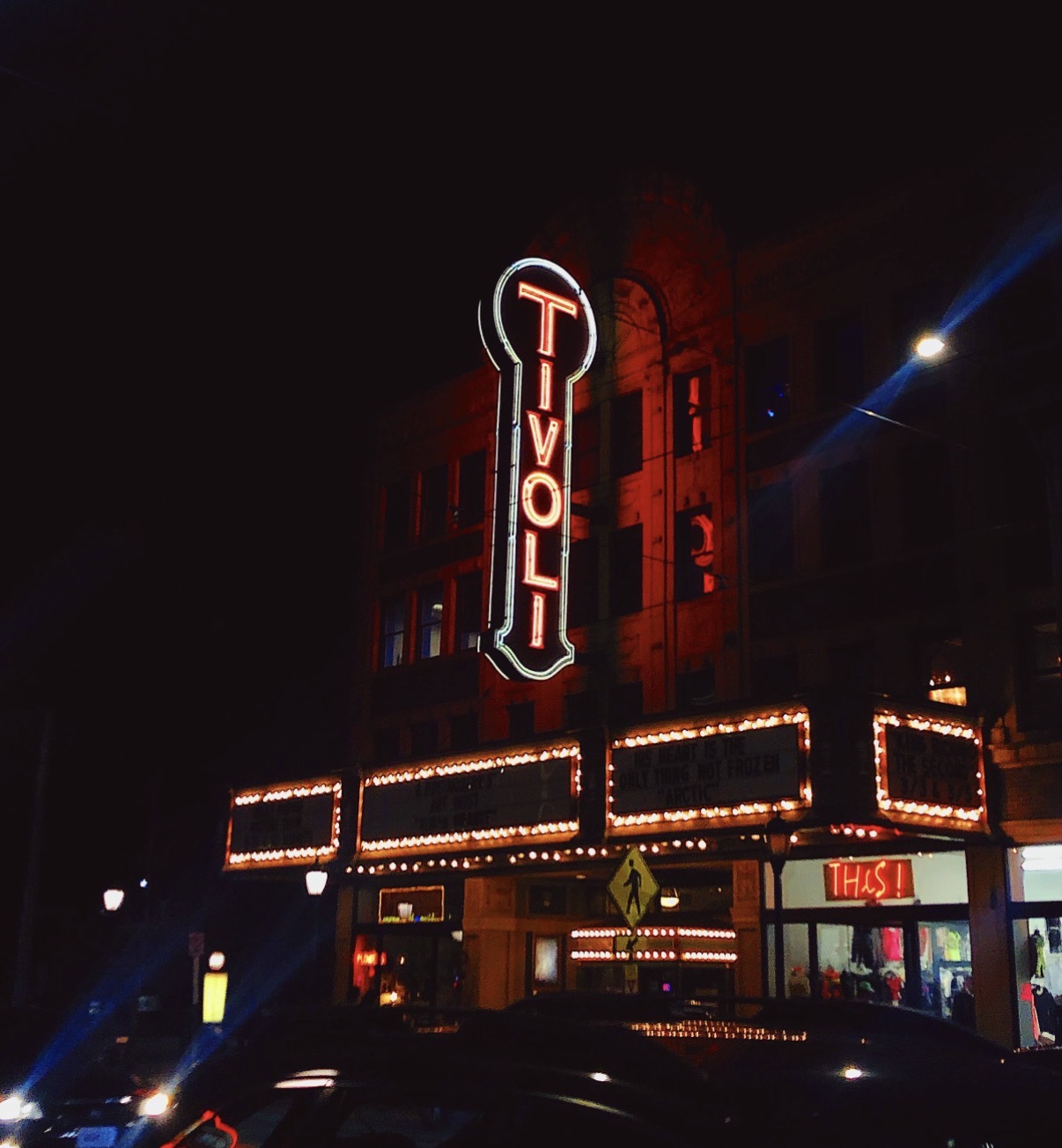 Night scene of a building with illuminated vertical and horizontal signs, including a large neon sign reading 'TIVOLI'.