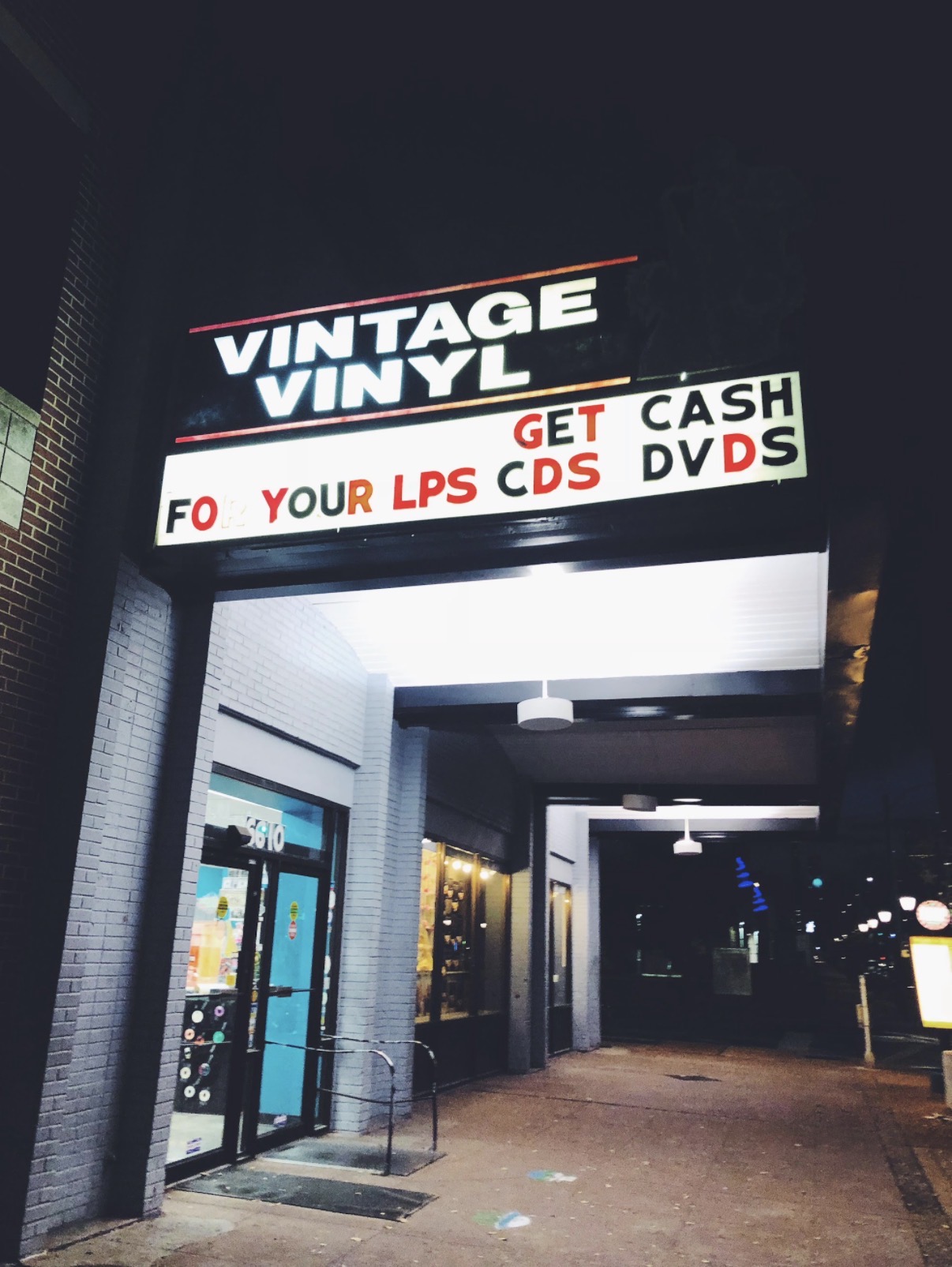 Storefront with a sign reading 'VINTAGE VINYL' and promotional text about LPS, CDs, cash, DVDs, and discounts.