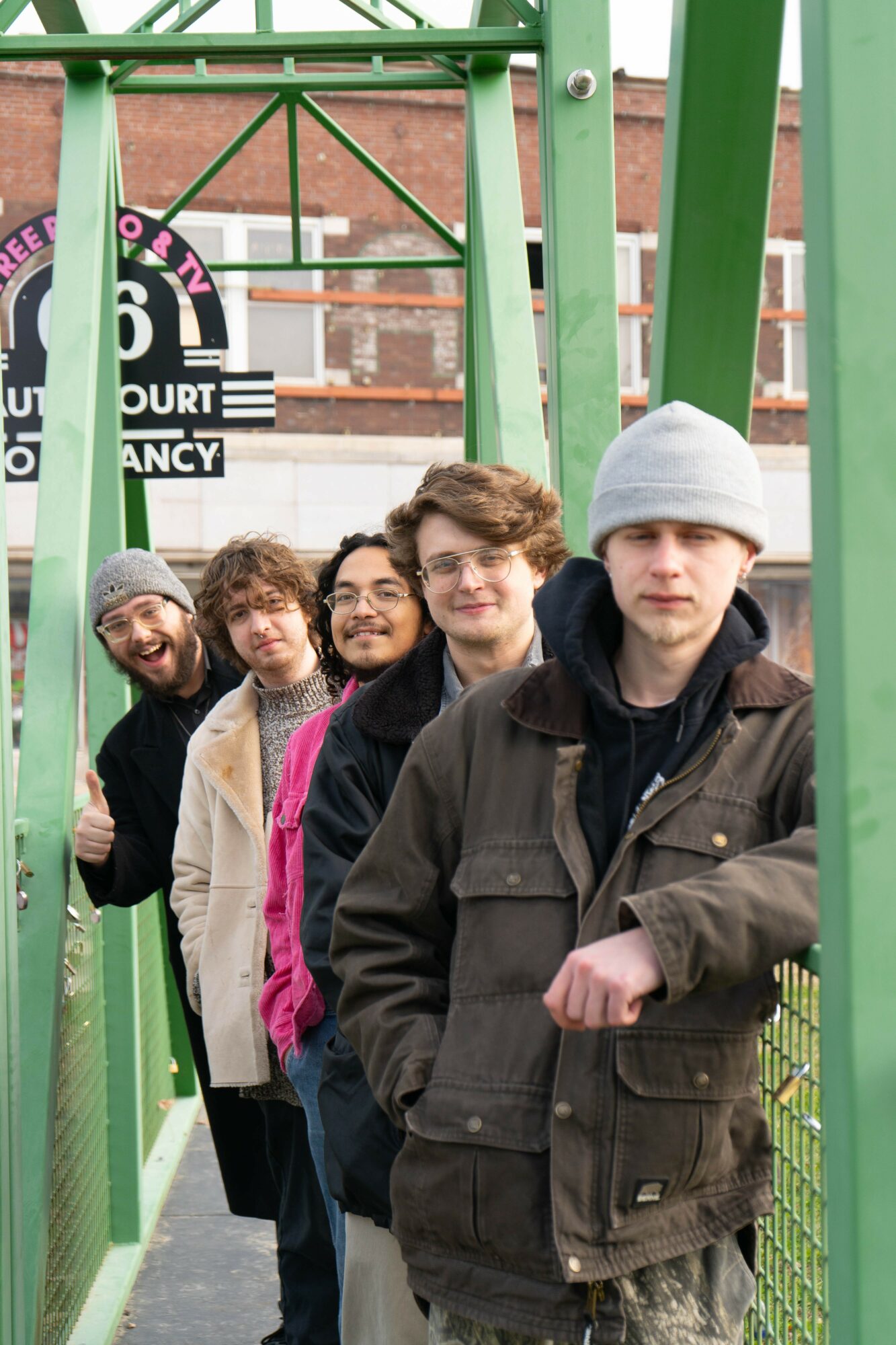 Five people standing in a line on a green playground structure, smiling and looking at the camera.