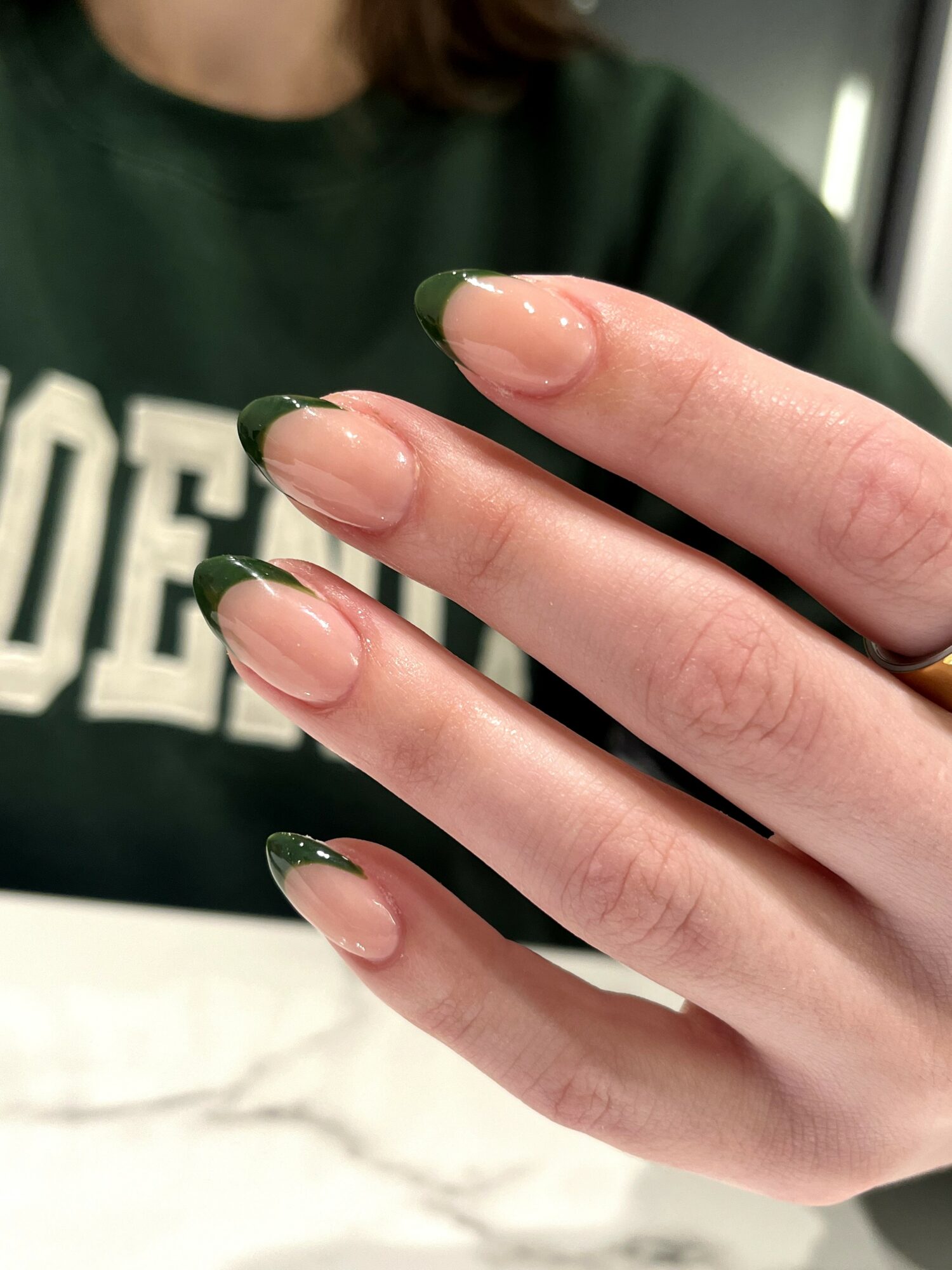 Close-up of a person's hand with nails painted green, fingers slightly spread, in front of a blurred background.