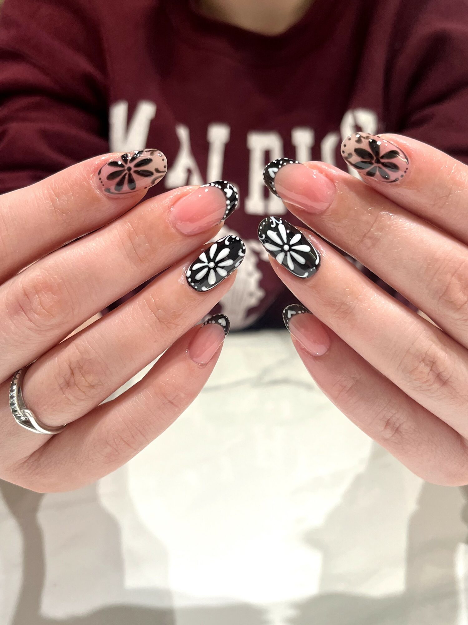 Person with black and white floral patterned nail art, holding their hands close together, wearing a maroon sweatshirt.