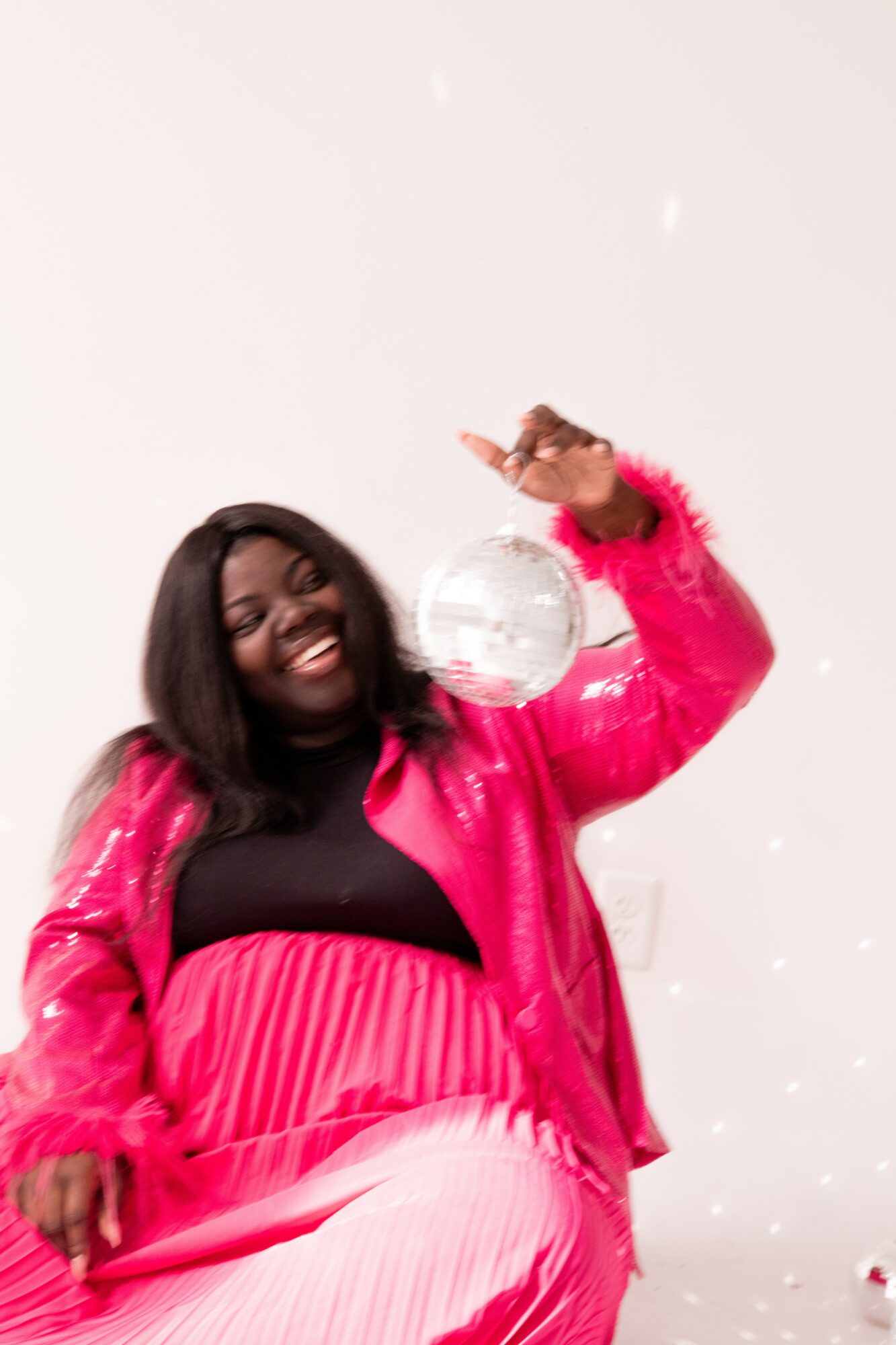 Person with long dark hair smiling, wearing a pink jacket and black top, holding a transparent ball, against a light background.