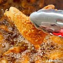Fried food being lifted from hot oil with tongs, crispy and golden brown, bubbling oil around.