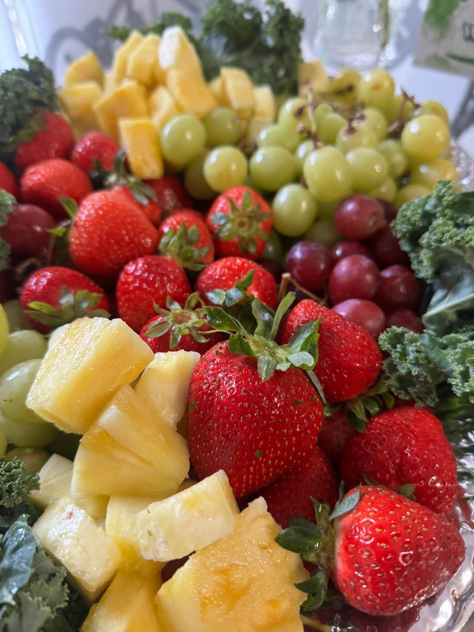 Assorted fresh fruits including strawberries, pineapple, green grapes, red grapes, and kale leaves.